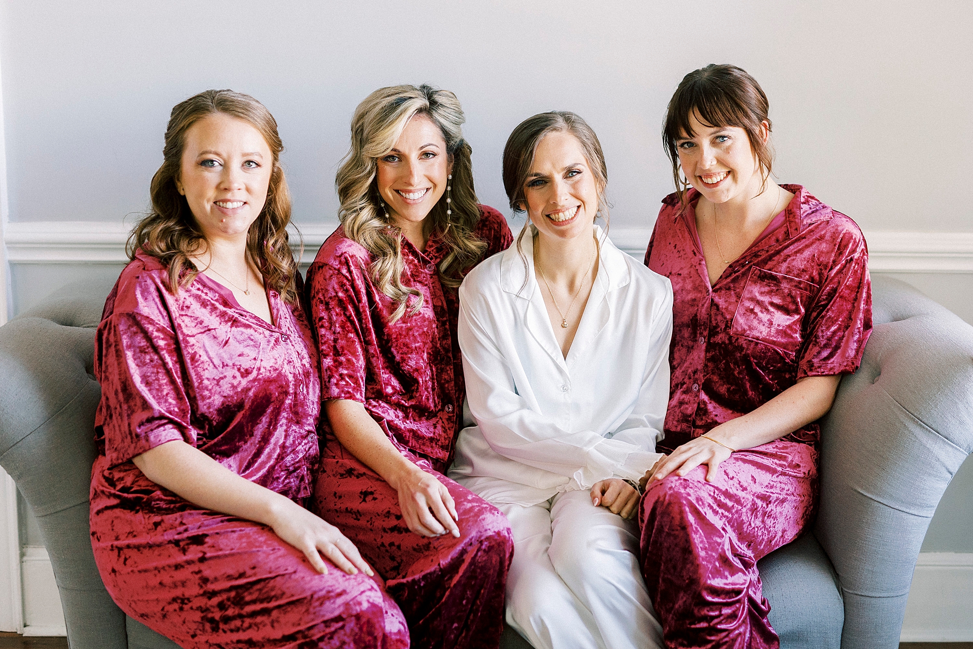 bride sits on couch with bridesmaids in burgundy pajamas