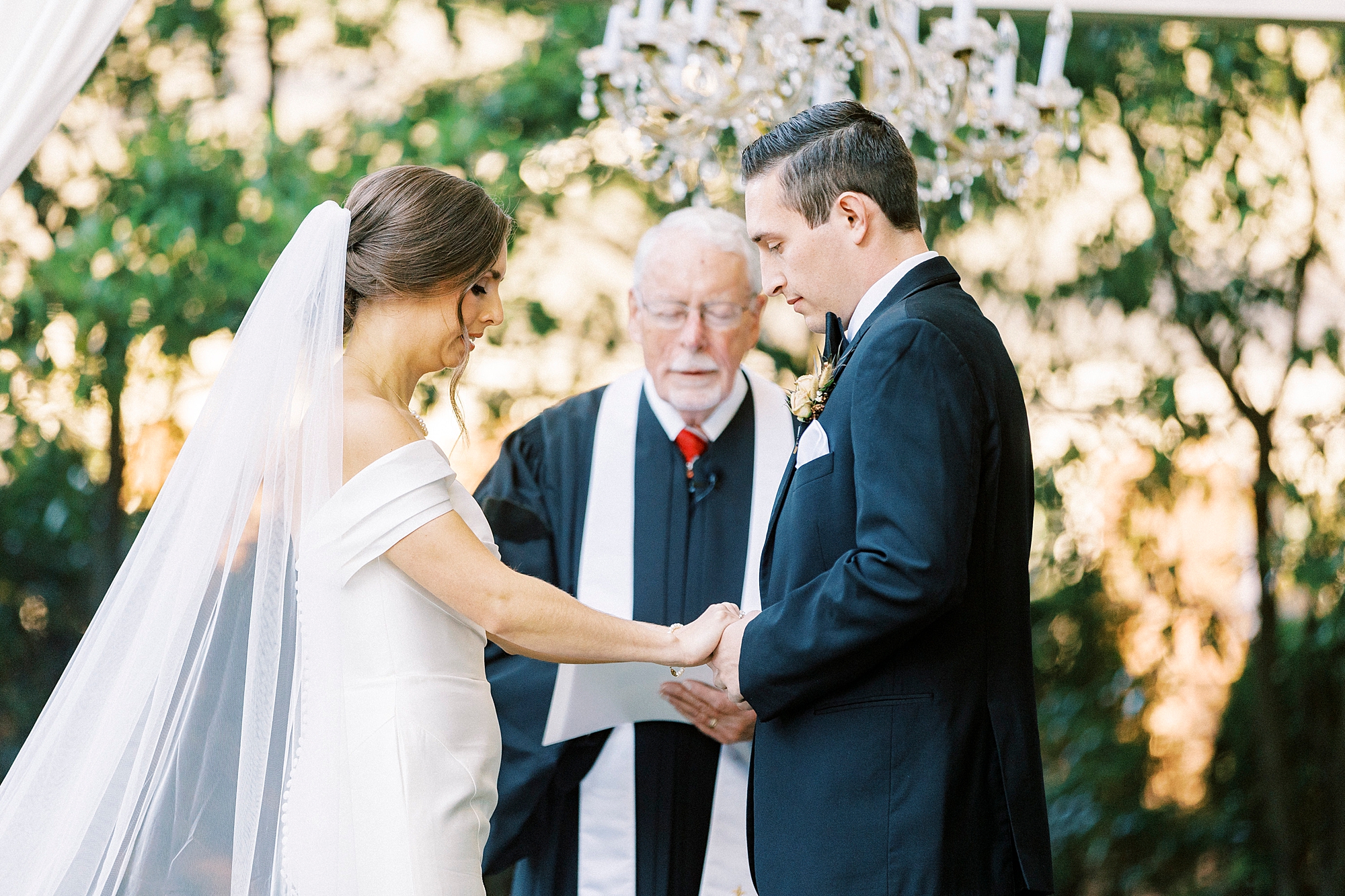 bride and groom hold hands bowing heads during outdoor ceremony at Separk Mansion