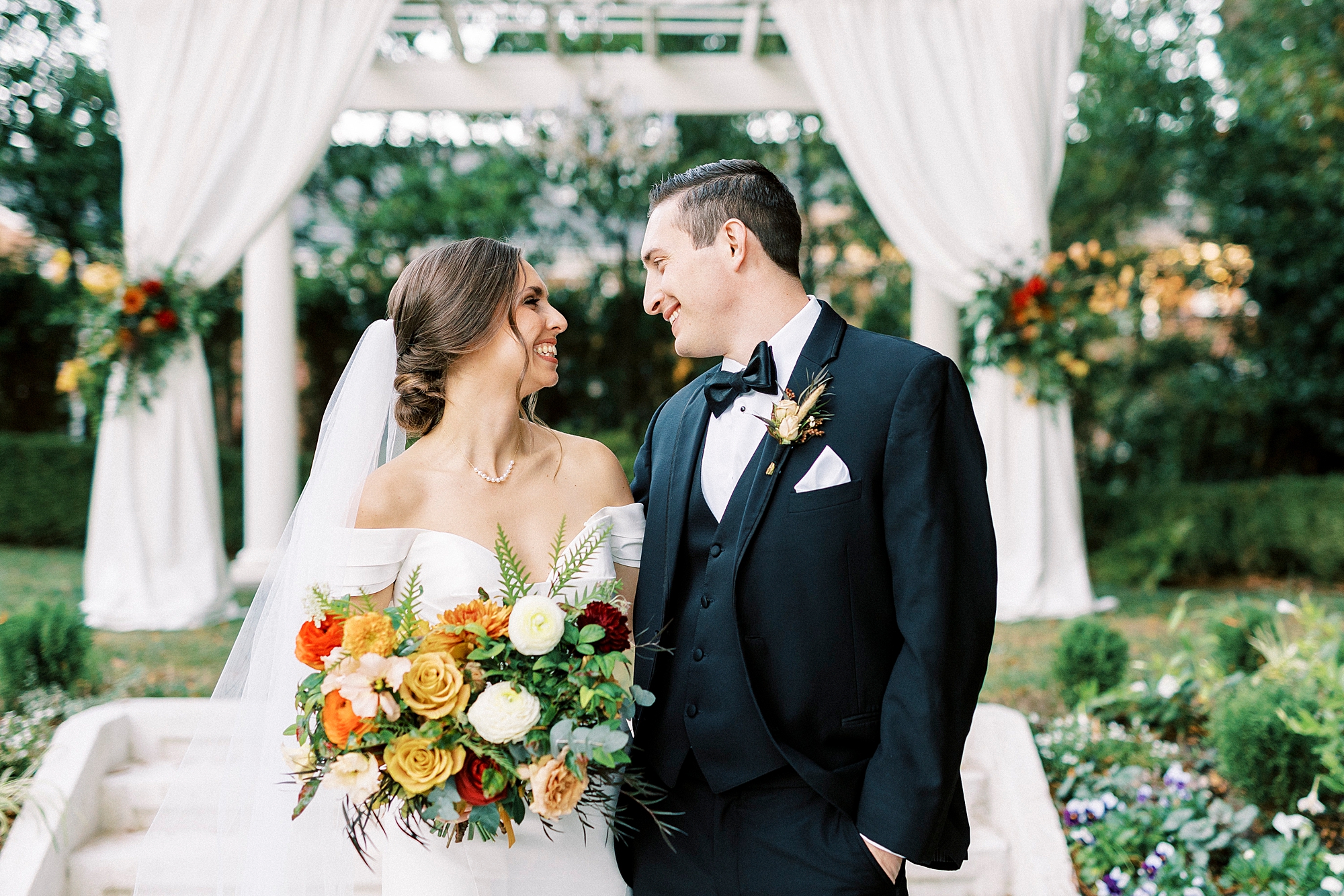 newlyweds smile in front of stone gazebo with white gauze