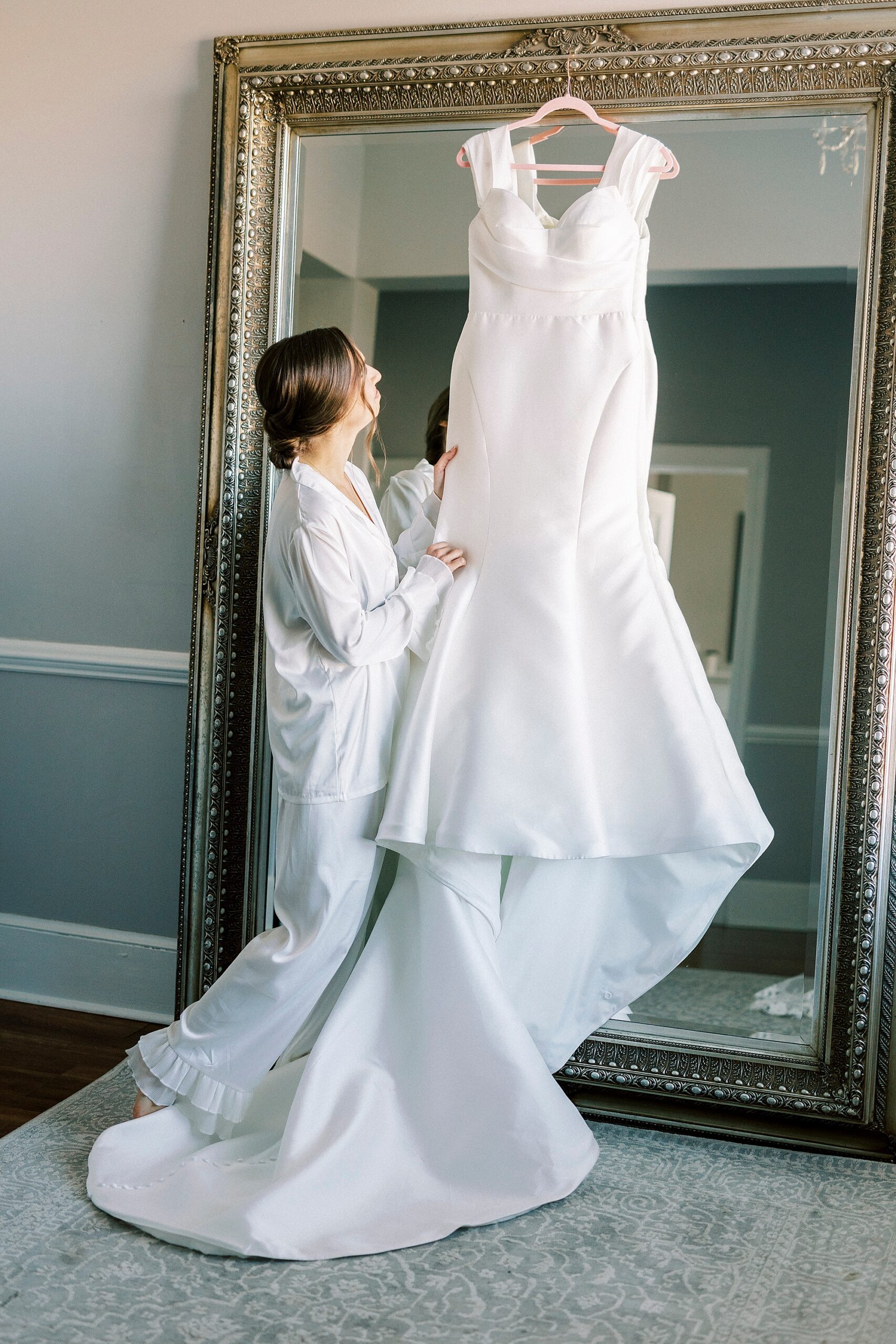 bride looks at wedding dress hanging on gold framed mirror inside Separk Mansion bridal suite