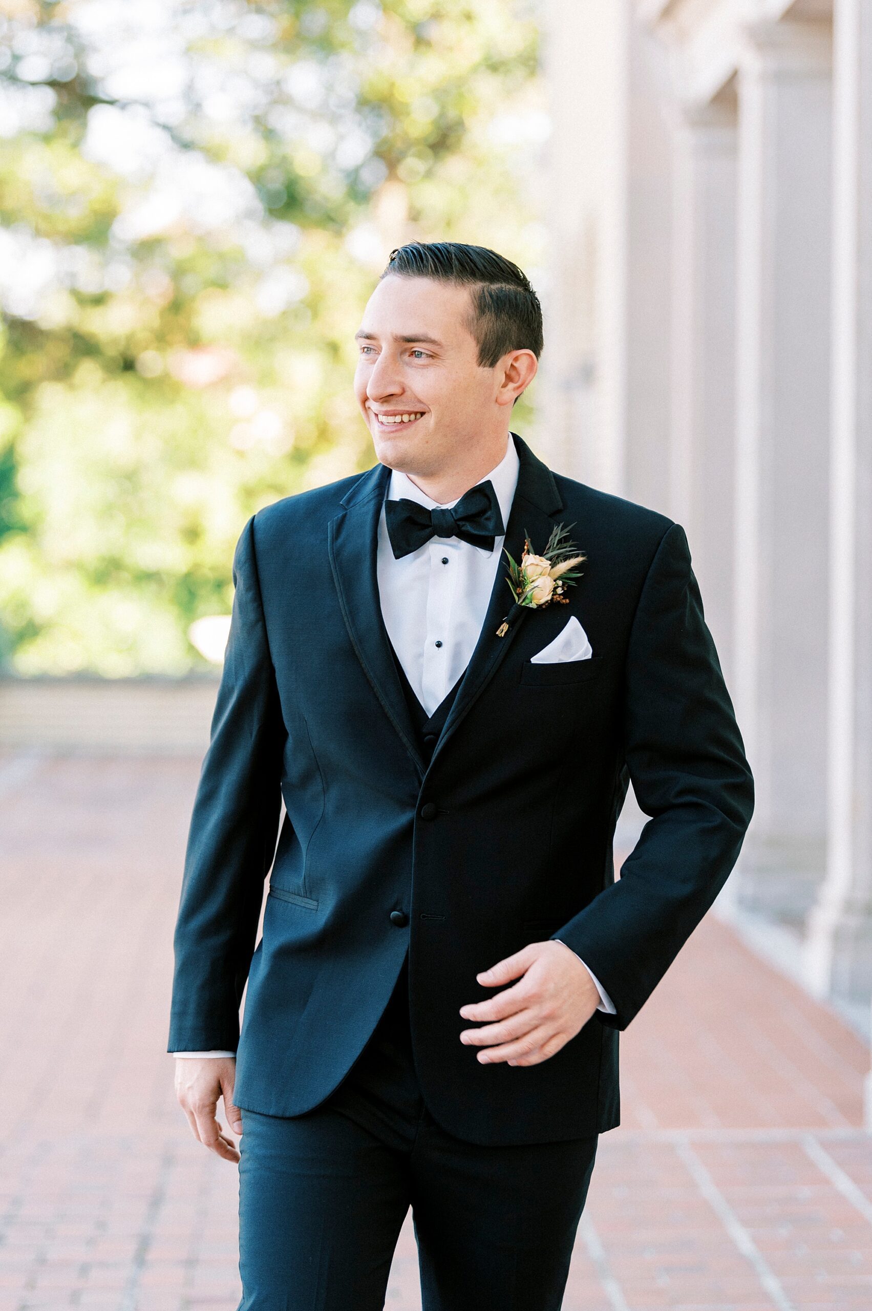groom stands with hand on pocket of black suit jacket