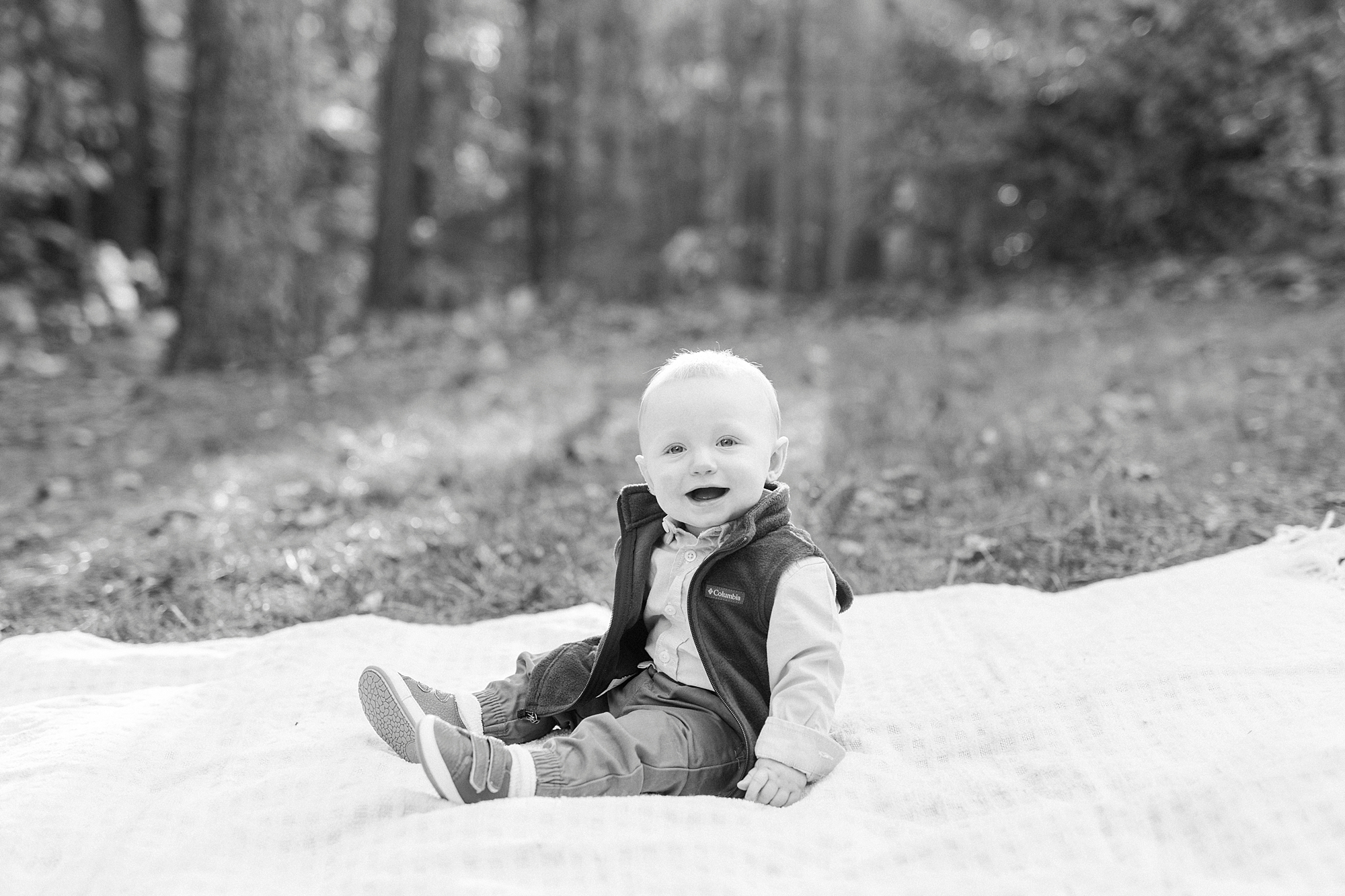 toddler in puffer jacket sits on white blanket during fall family portraits at Charlotte home