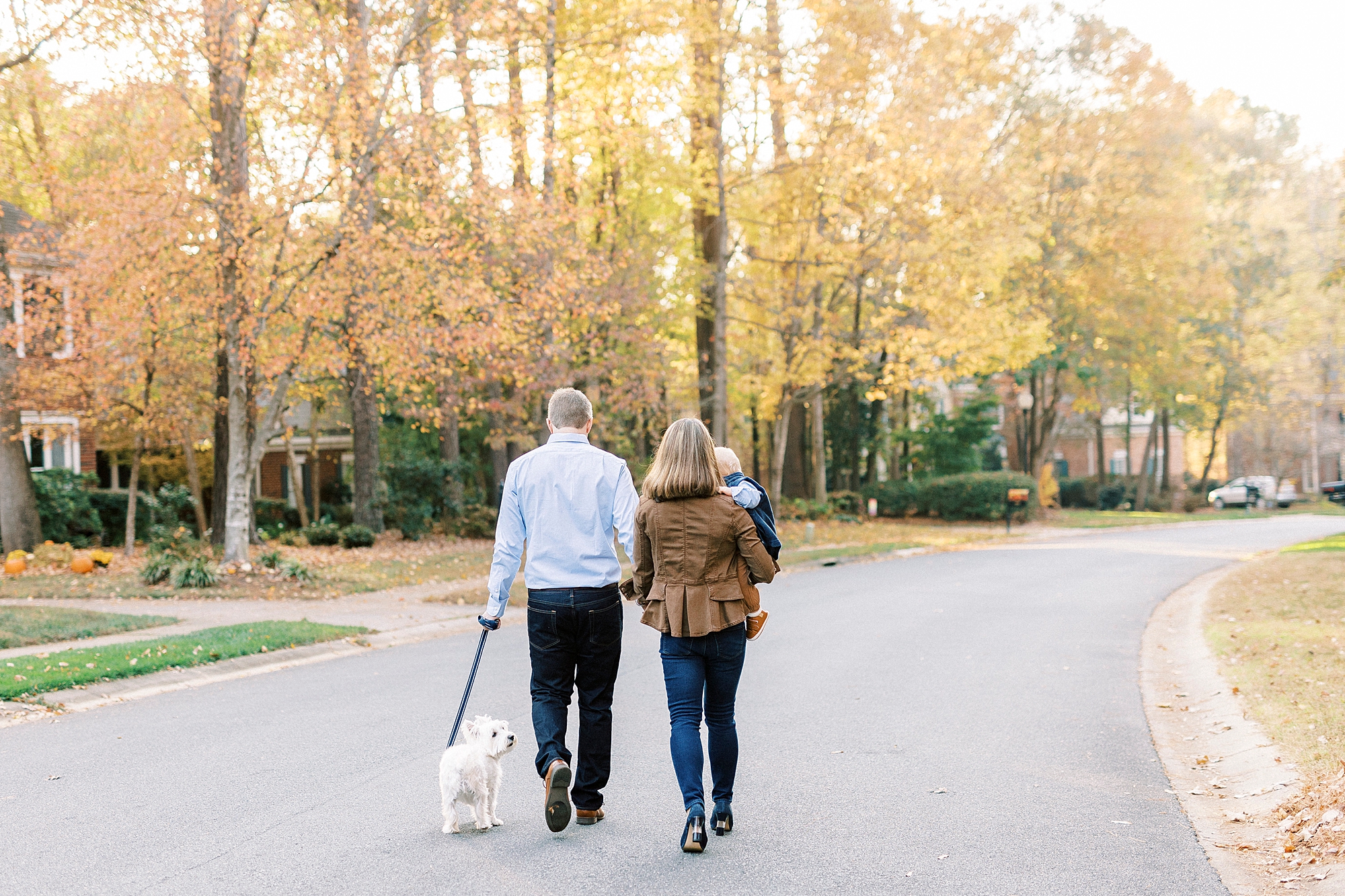 family walks carrying son while walking dog on street outside home 