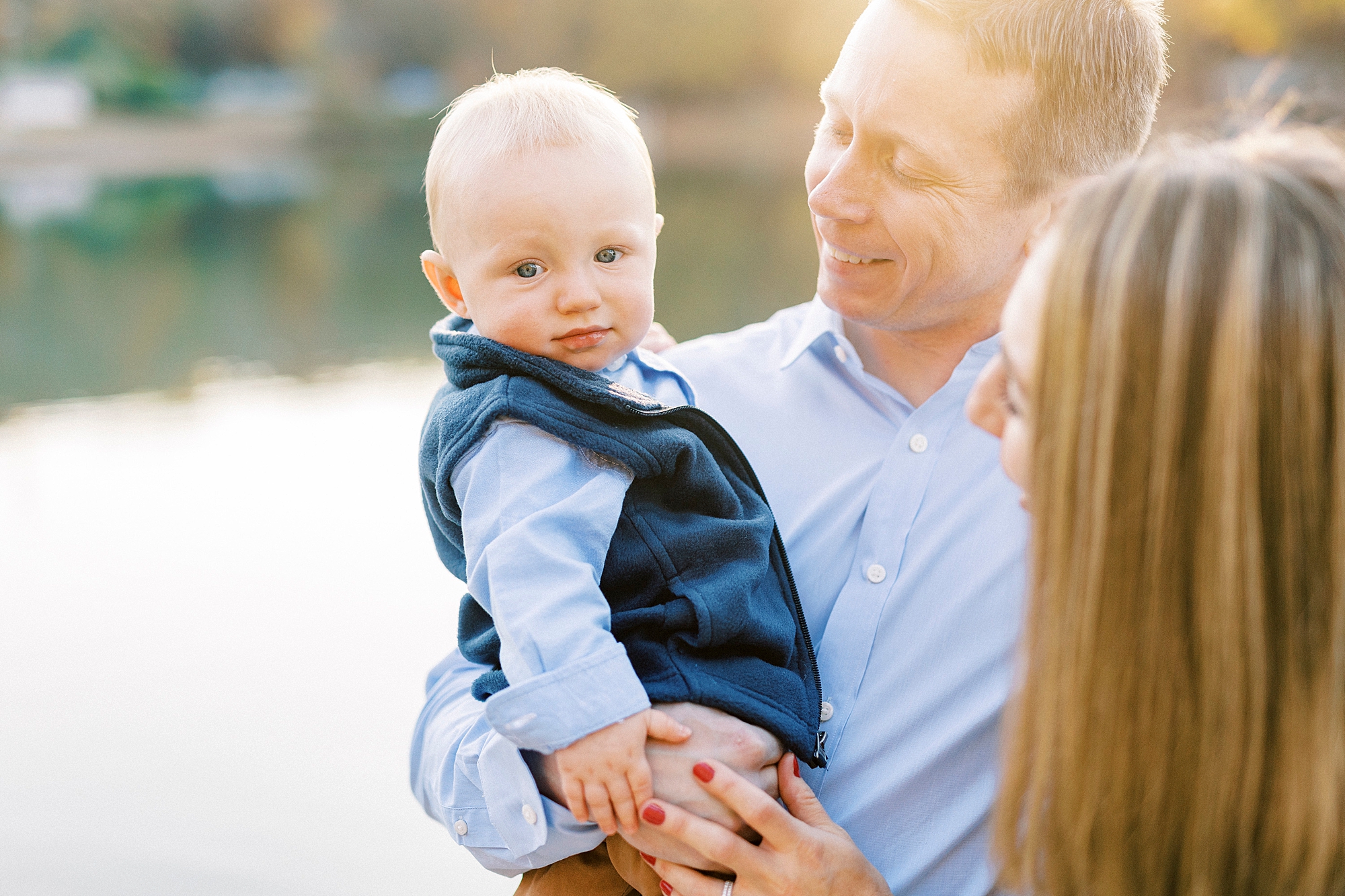 baby makes silly face while dad looks at him near water 