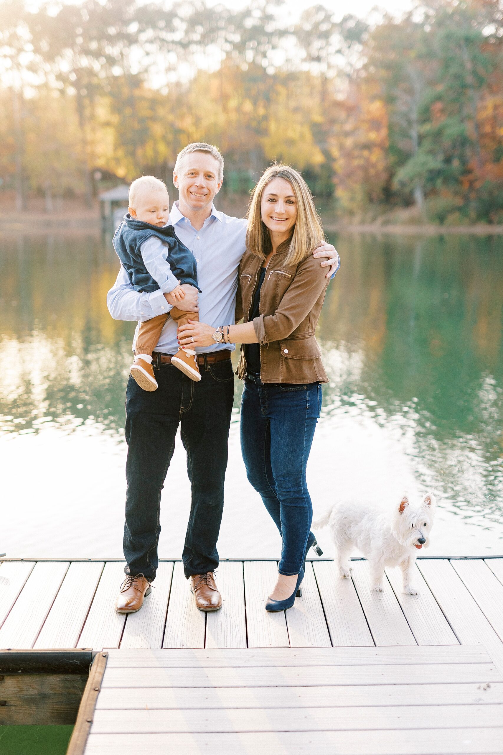 parents hug with son on dad's hip in front of lake in Charlotte NC