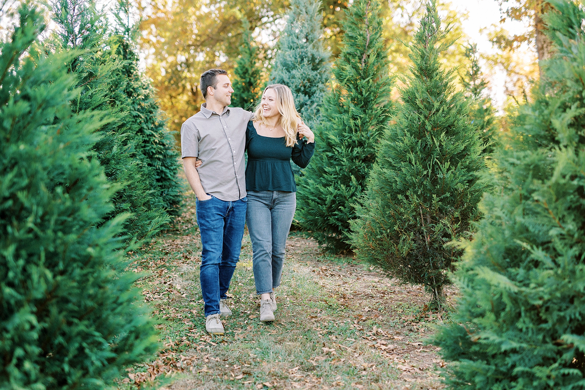 couple holds hands running through a row of Christmas trees