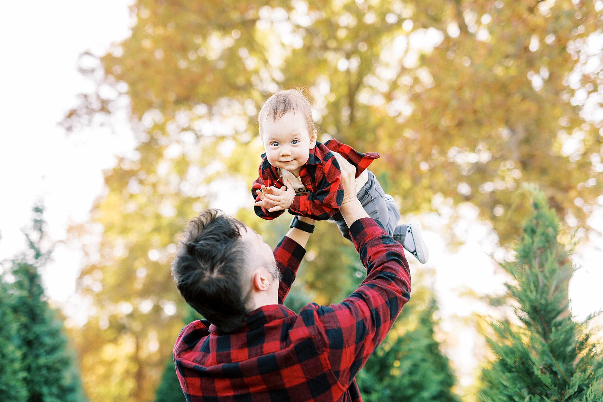 dad in buffalo plaid shirt lifts up baby in buffalo plaid shirt