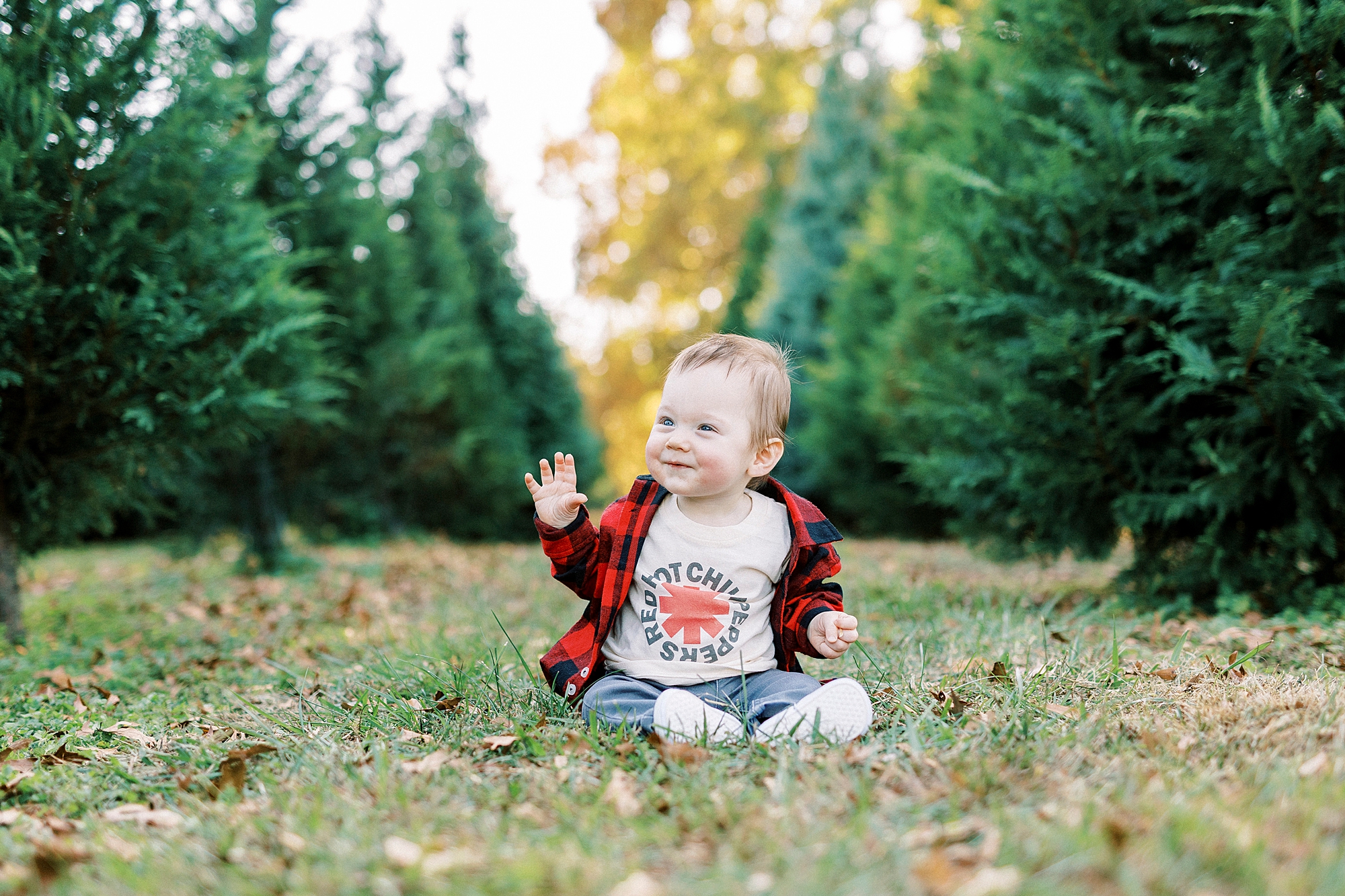 baby sits between trees waving during Almond Christmas Tree Farm mini sessions
