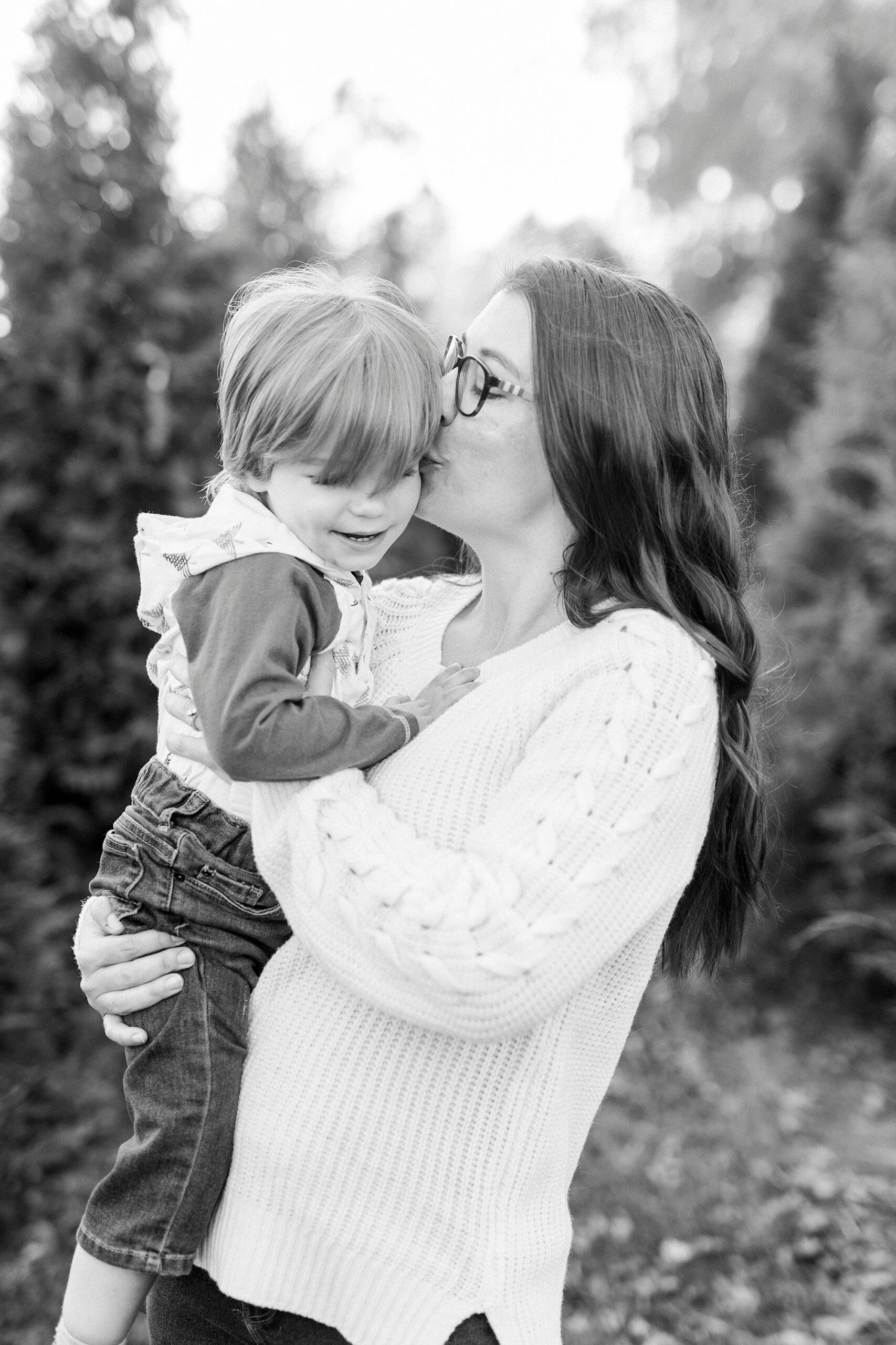 mom in white sweater kisses baby boy on cheek during Almond Christmas Tree Farm mini sessions