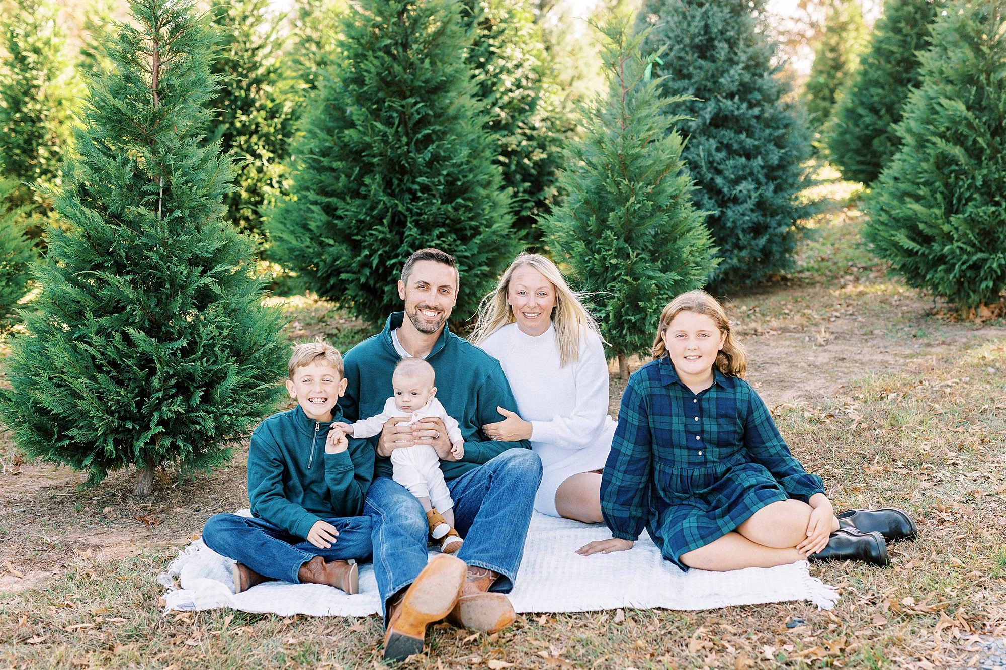 family of five sits on blanket in front of Christmas trees at Almond Christmas Tree Farm