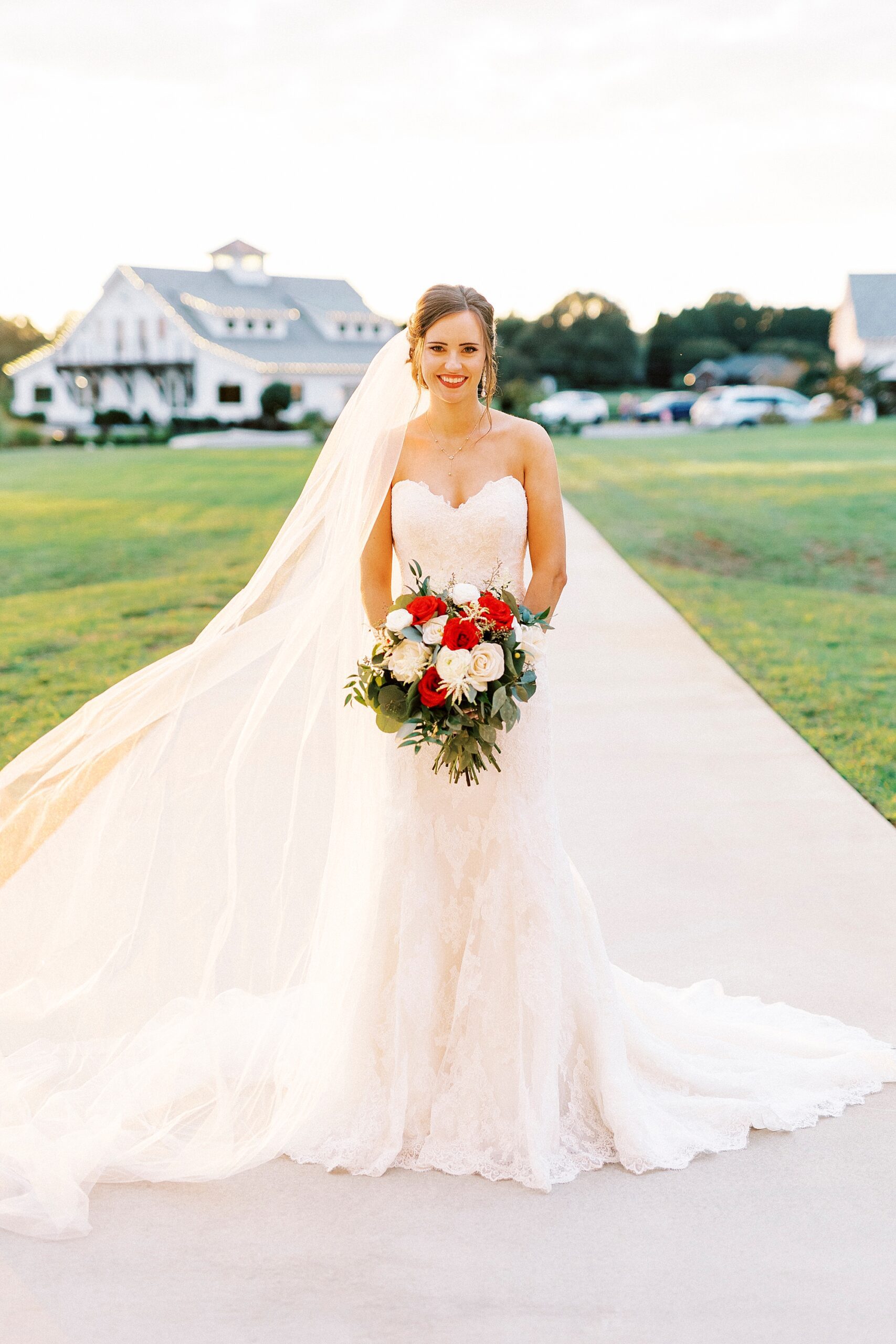 bride holds bouquet of white and red flowers with veil around her 