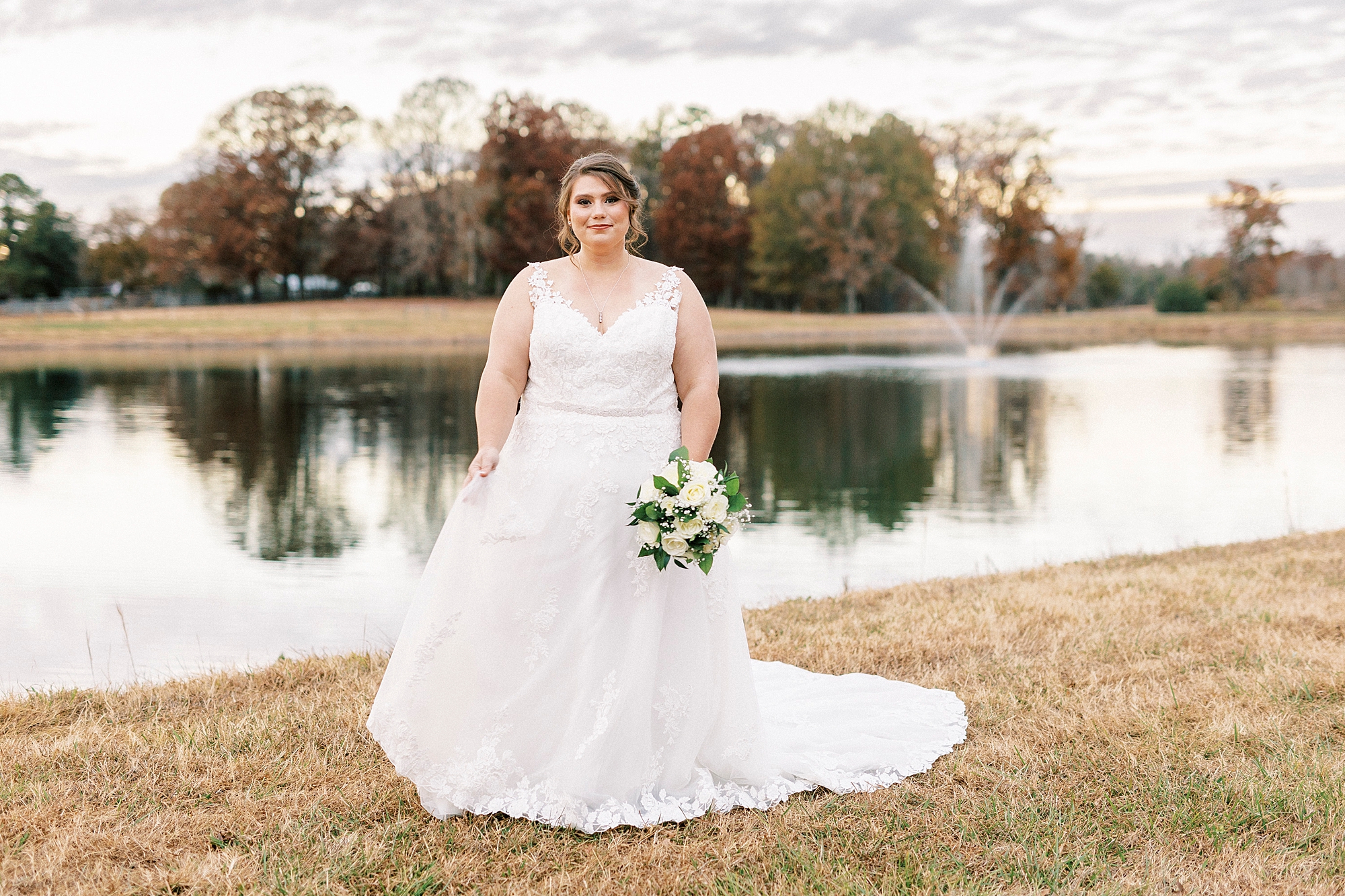 bride stands holding bouquet down next to hip near pond at the Farm at Brusharbor