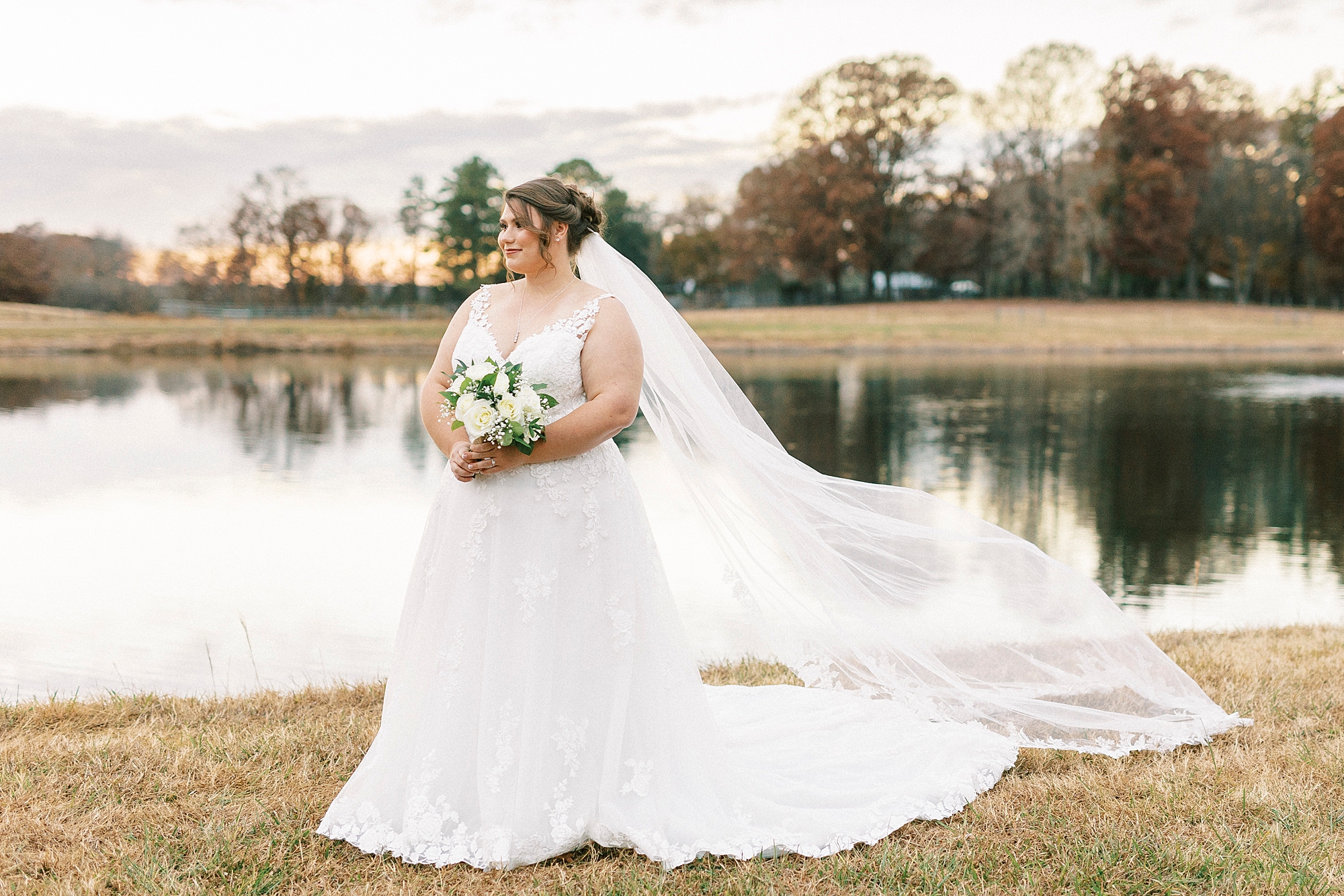 bride smiles looking over shoulder with veil trailing behind her near pond