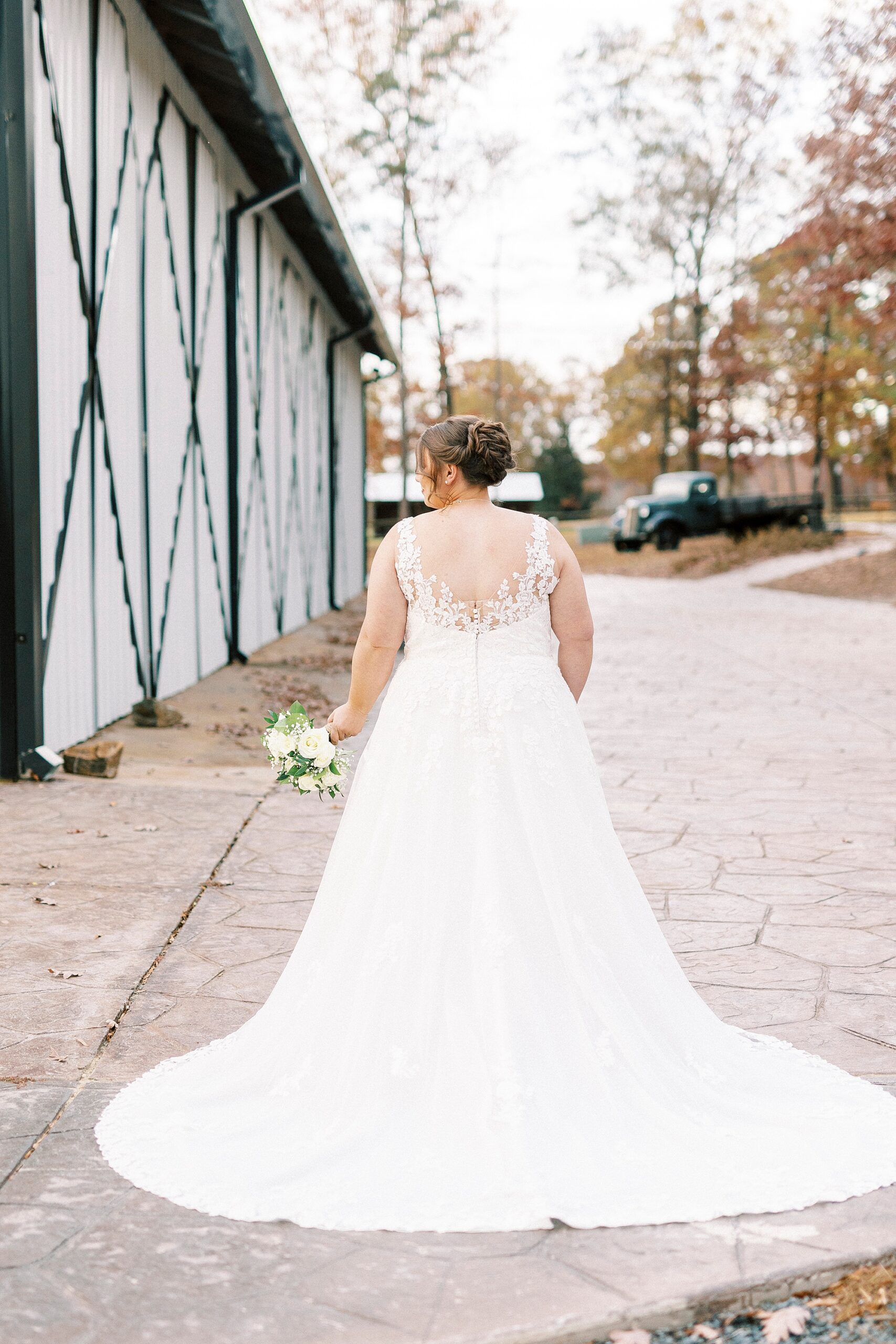 bride stands with bouquet next to her showing off back of wedding gown