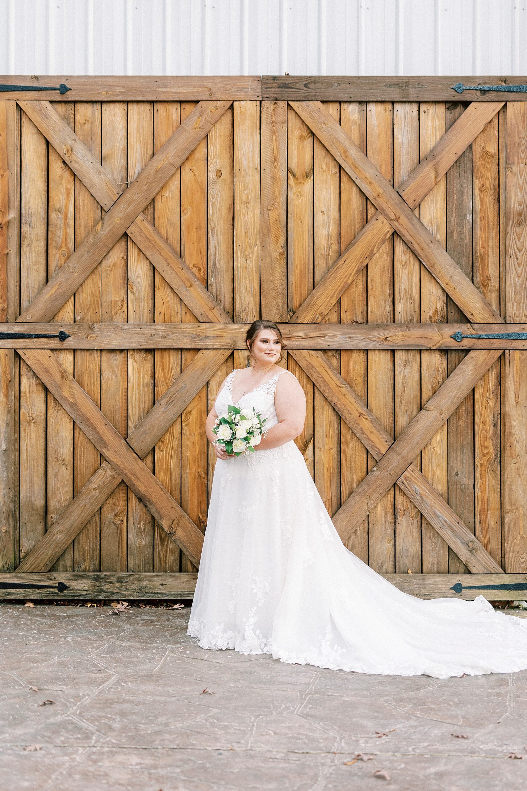 bride poses in front wooden barn doors and looks over her shoulder