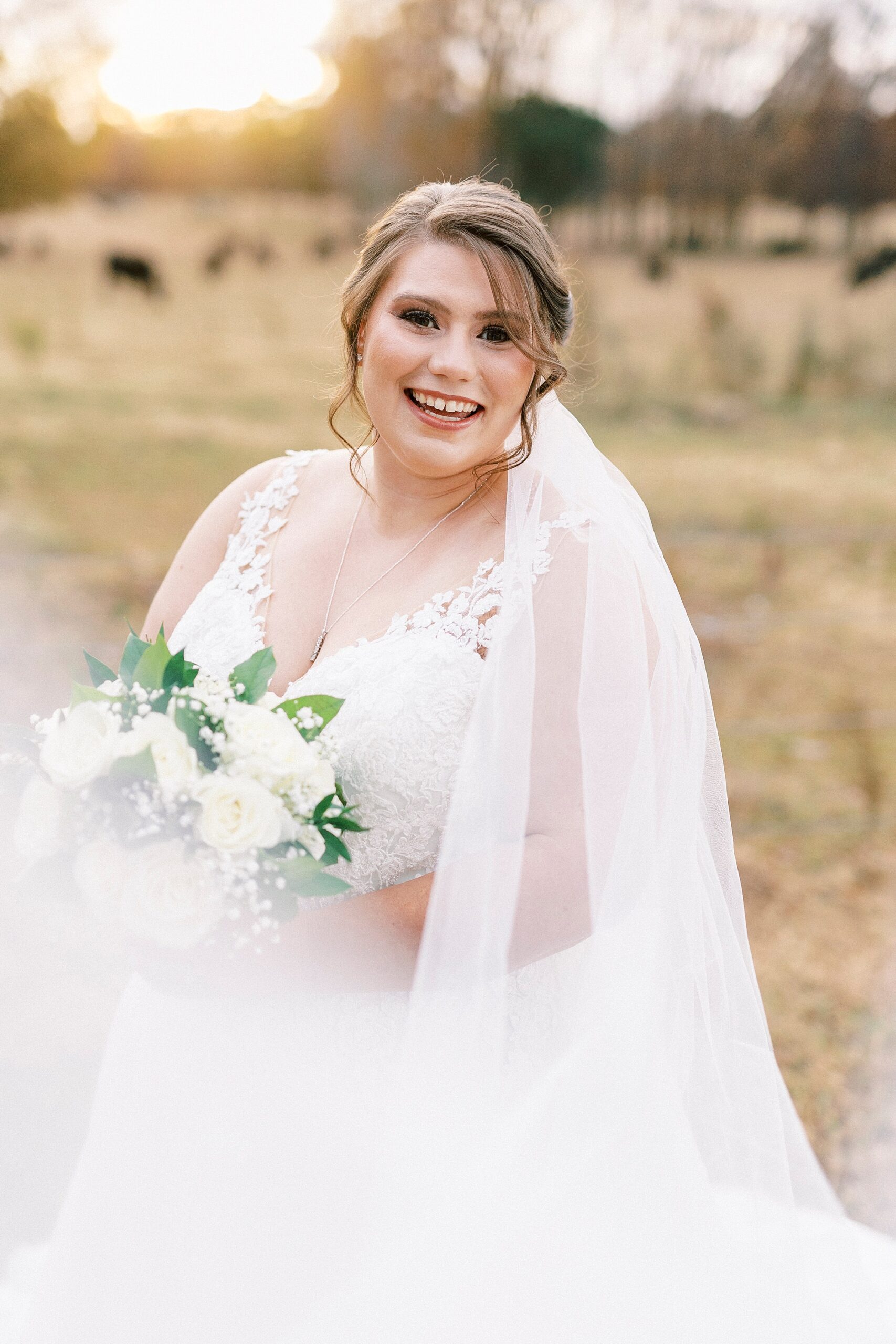 bride grins smiling over her shoulder with veil around her holding bouquet of white flowers