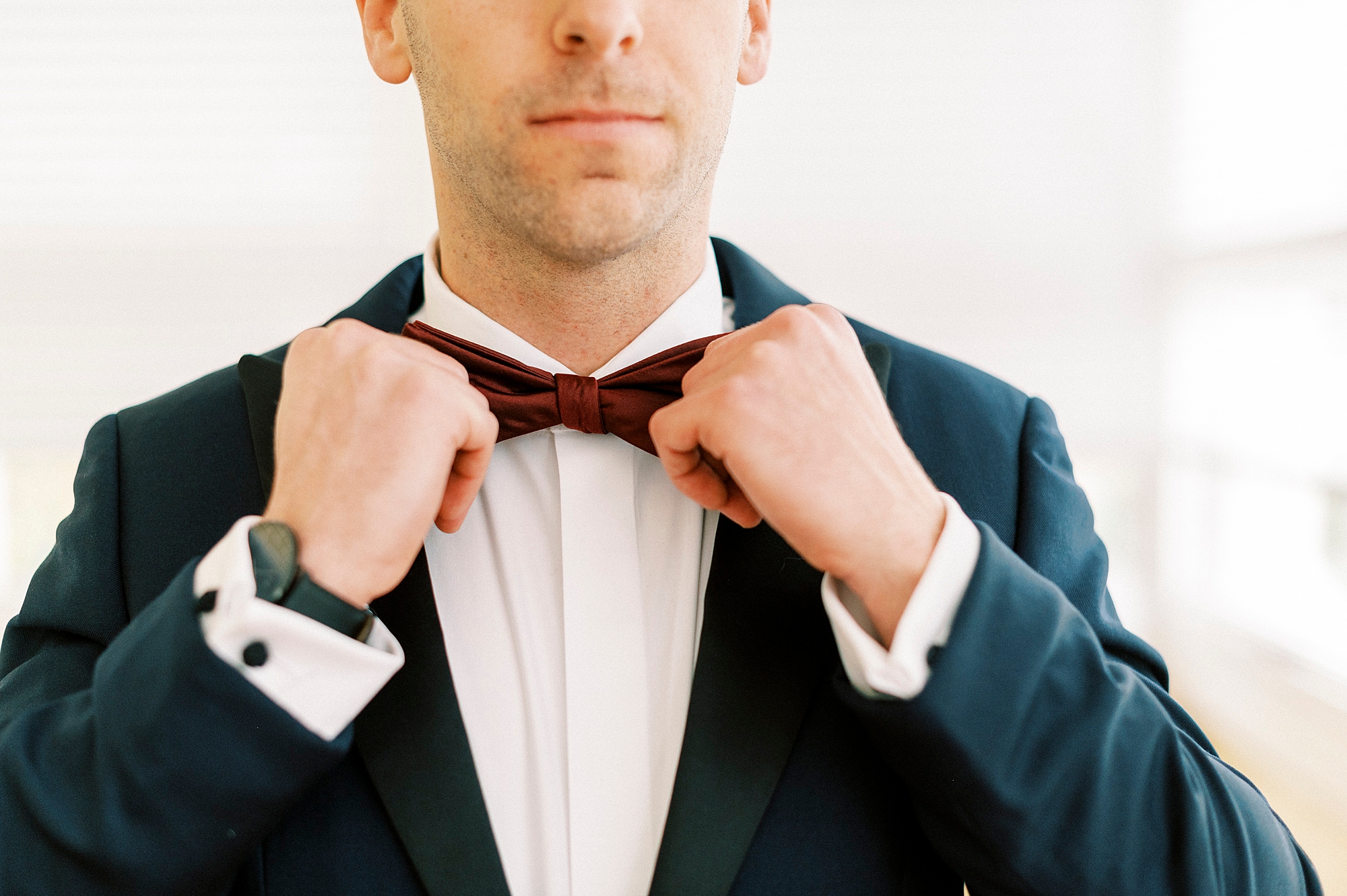 groom adjusts red bowtie during winter wedding prep