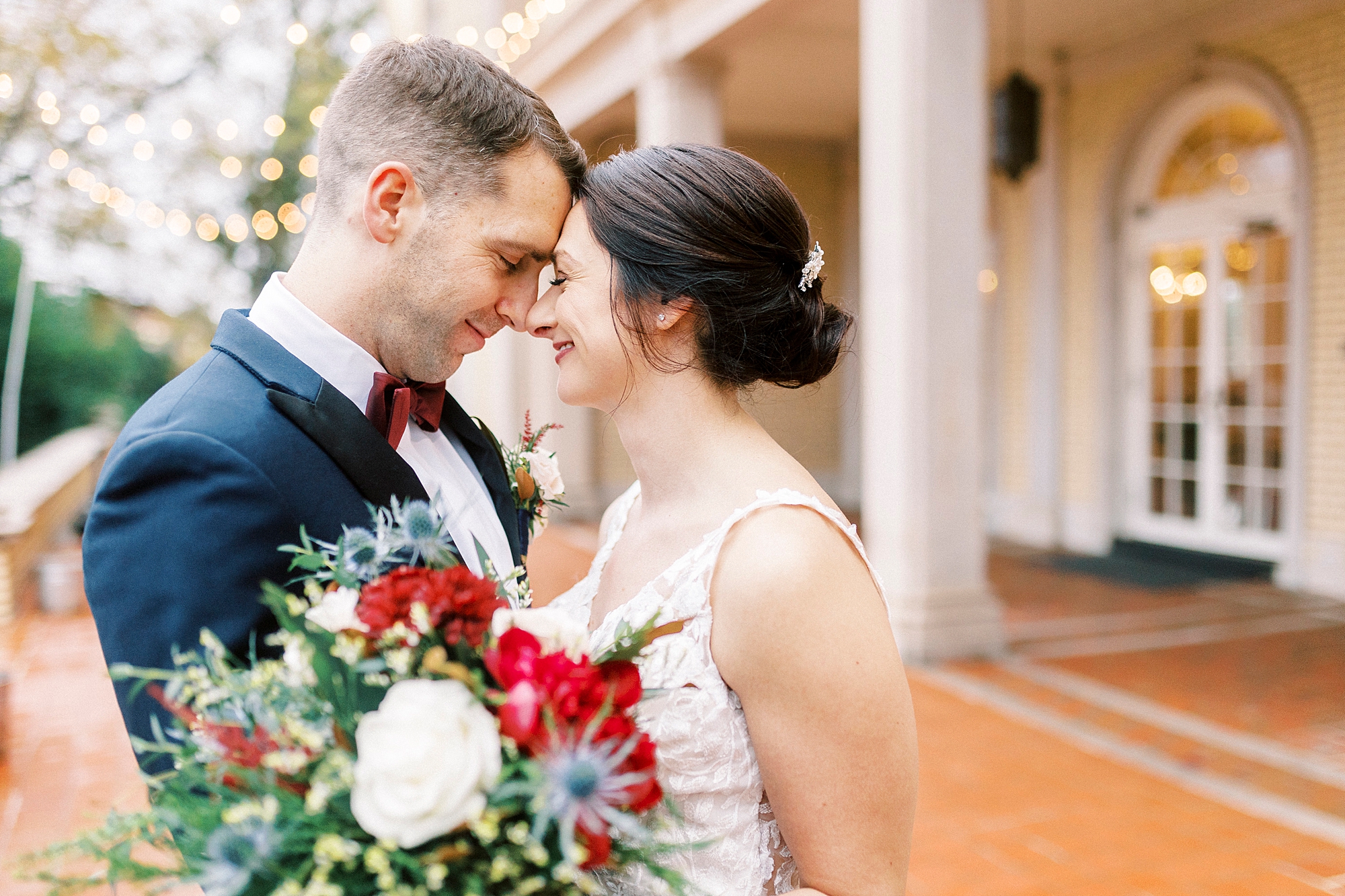 bride and groom lean heads together holding red and white bouquet