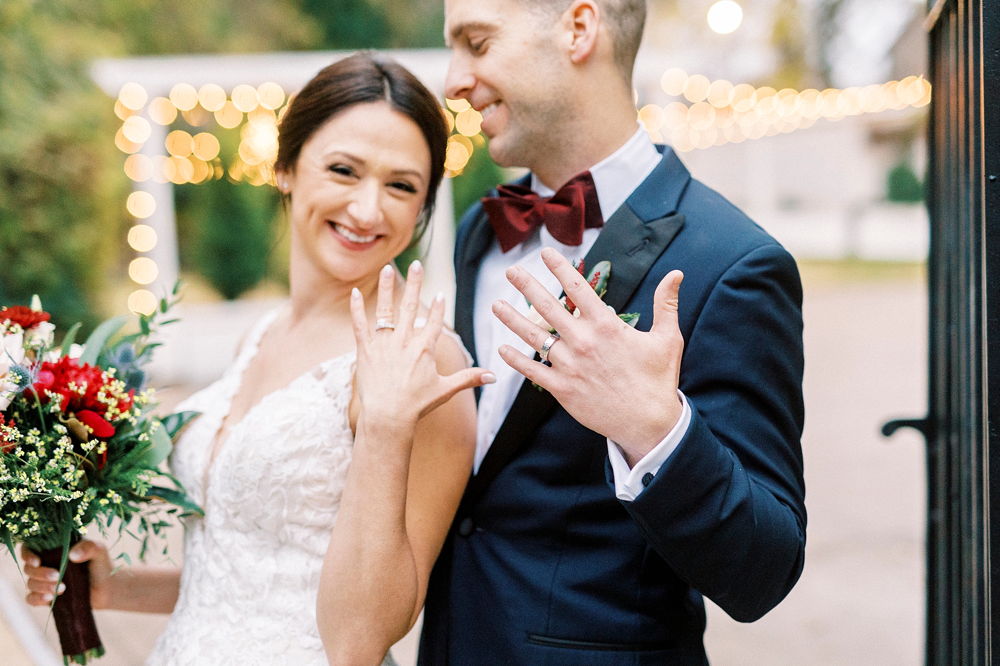 bride and groom smile laughing and holding up hands showing off wedding rings