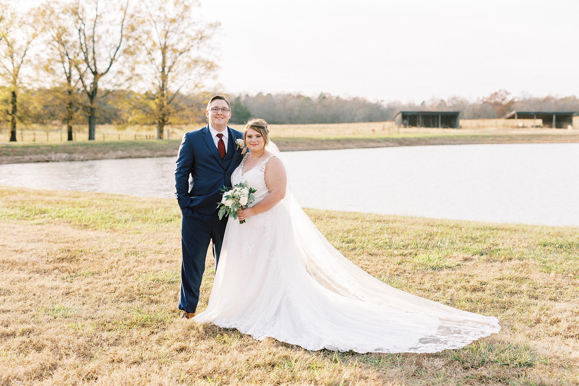 newlyweds hug near pond at the Farm at Brusharbor with cows behind them