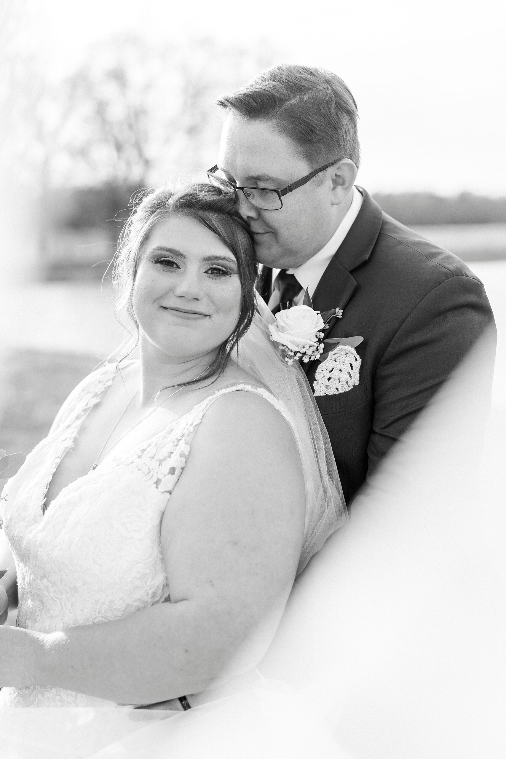 groom nuzzles bride's head near pond with veil floating around them at the Farm at Brusharbor