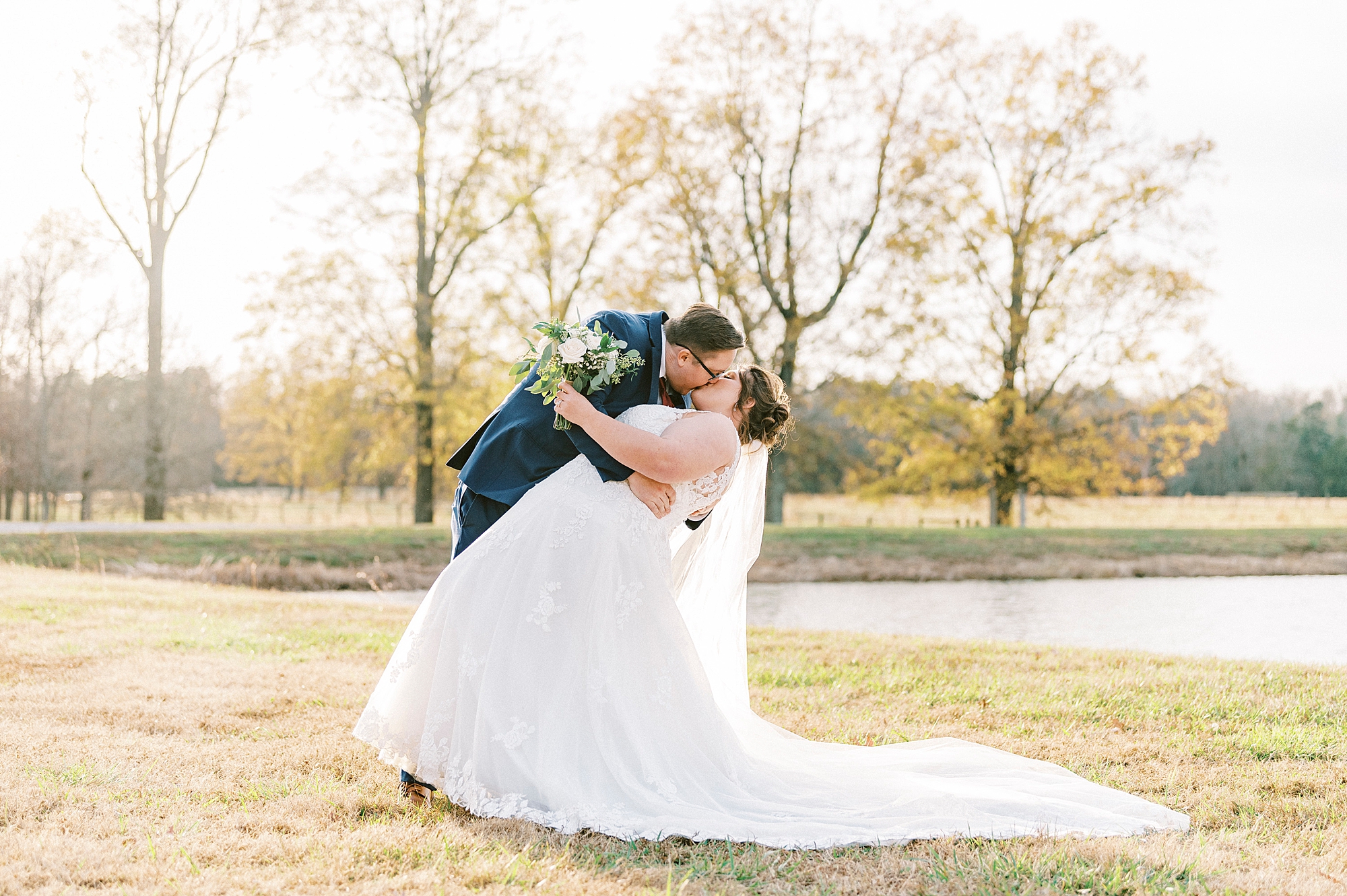 groom dips bride kissing her near pond at the Farm at Brusharbor