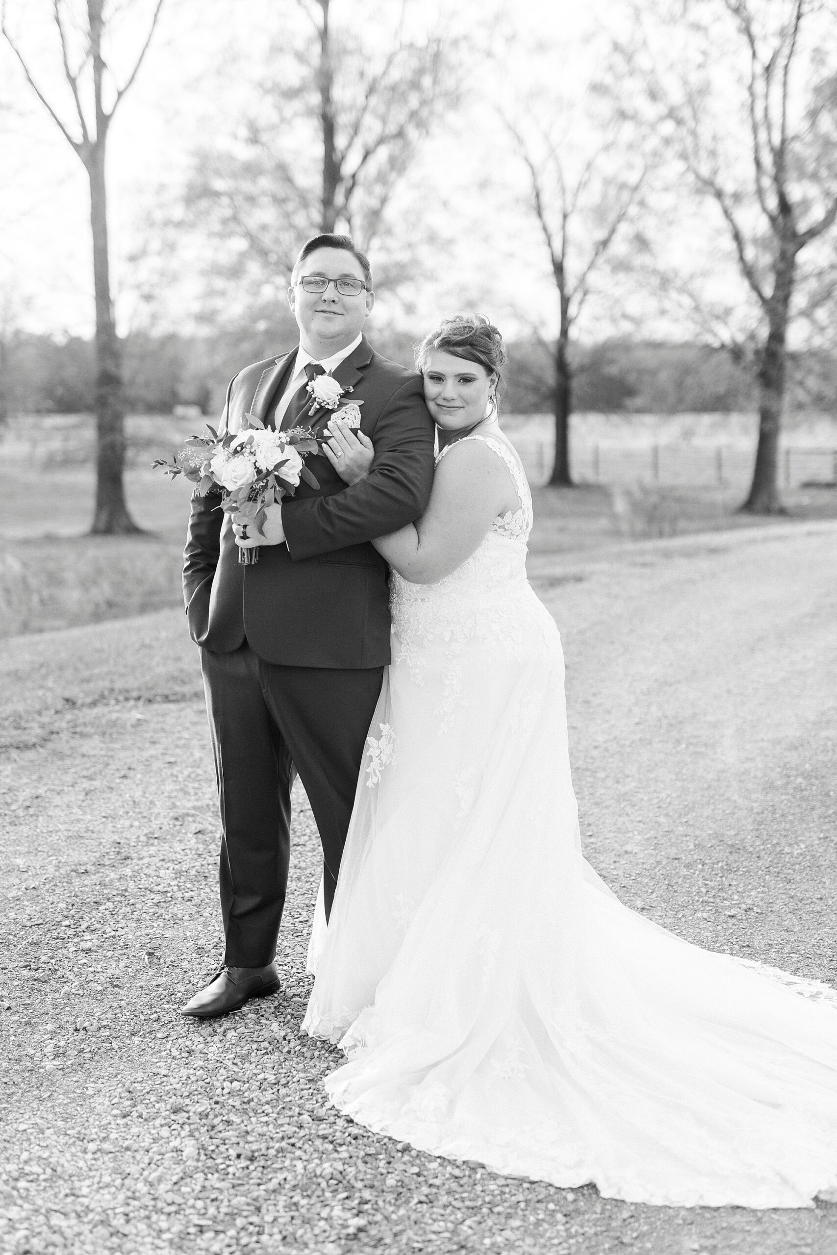 bride hugs groom from behind on driveway at the Farm at Brusharbor