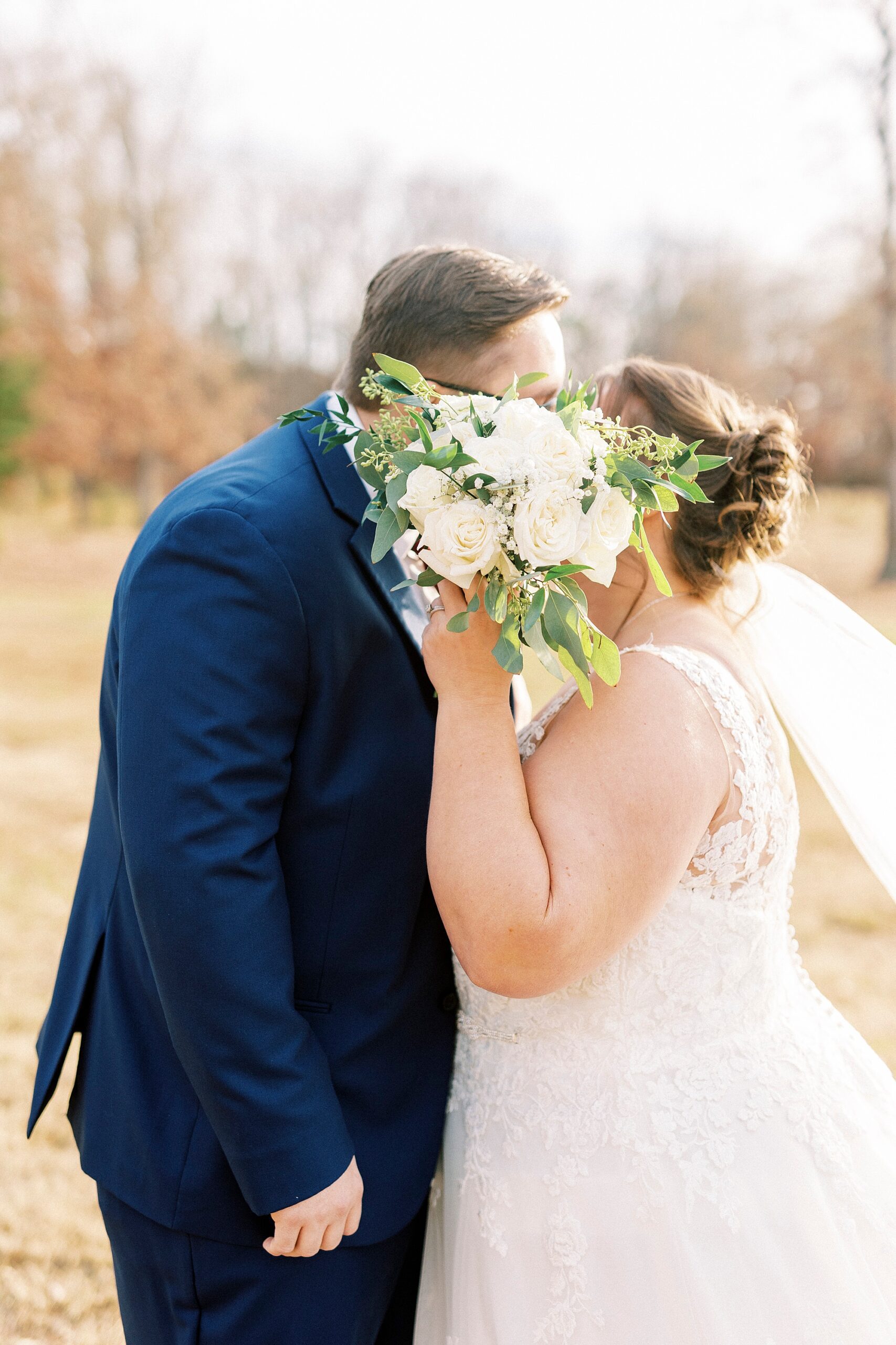 bride and groom kiss behind white bouquet on lawn at the Farm at Brusharbor