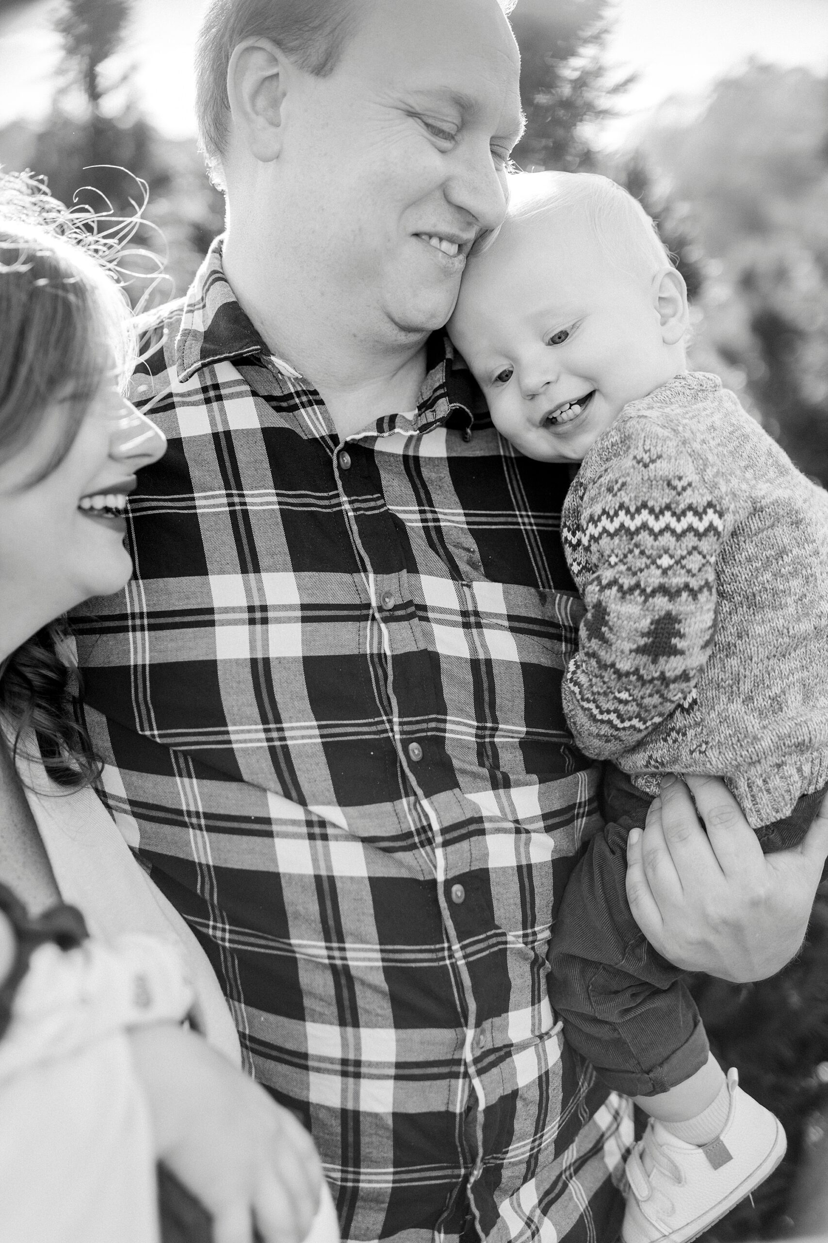 dad hugs toddler to his chest while mom holds arm during Penland Christmas Tree farm mini sessions 