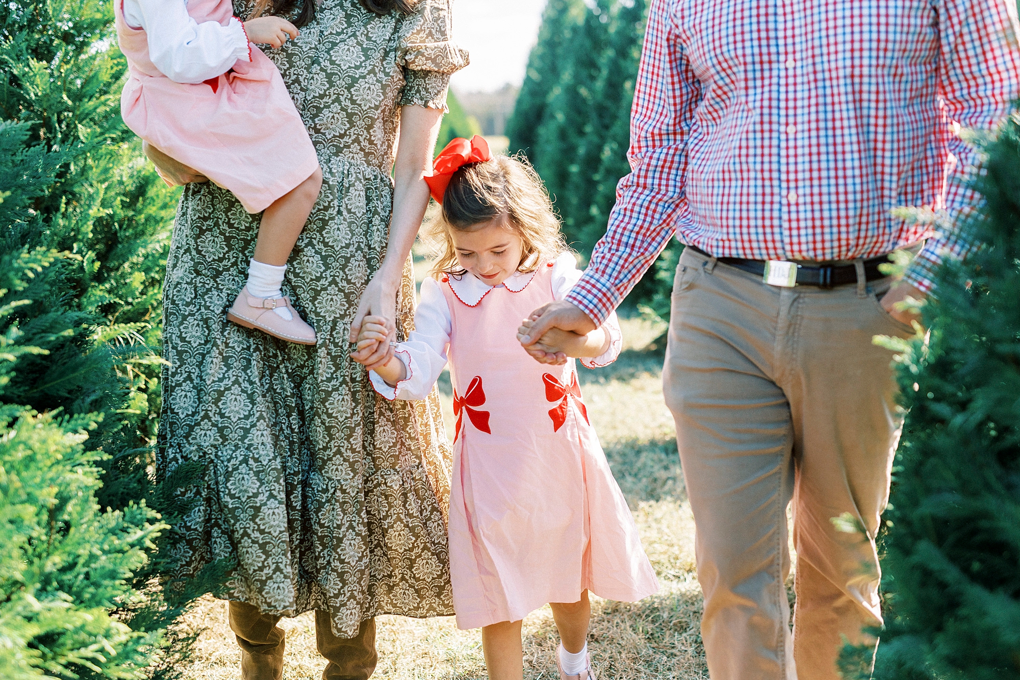 parents hold daughters hand while carrying second daughter on hip 