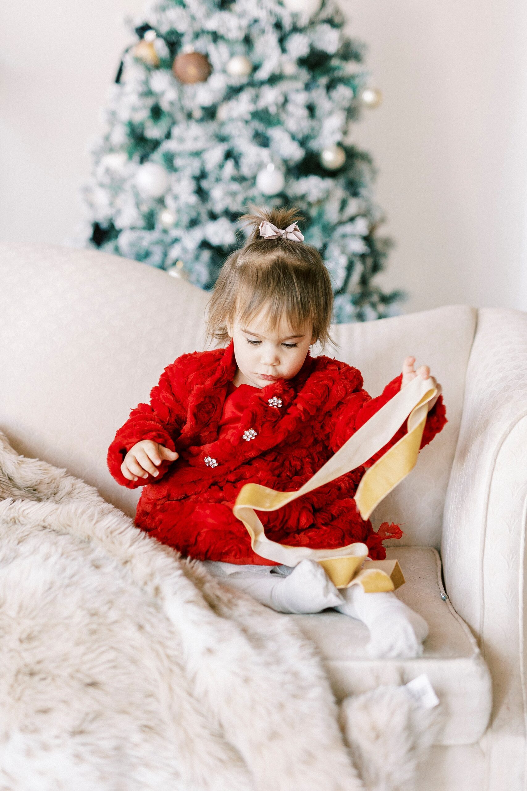 girl in red dress plays with ribbons during Christmas portraits in Downtown Concord studio