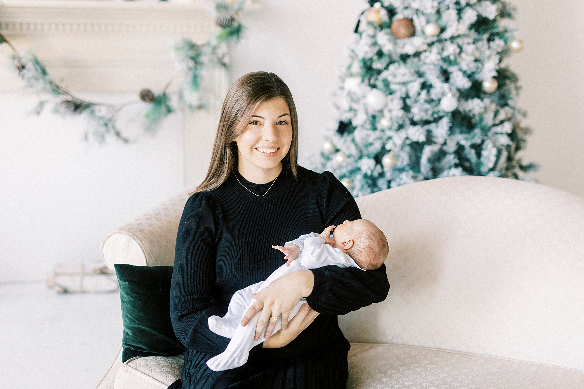 mom sits on ivory couch holding son during studio Christmas portraits in Downtown Concord
