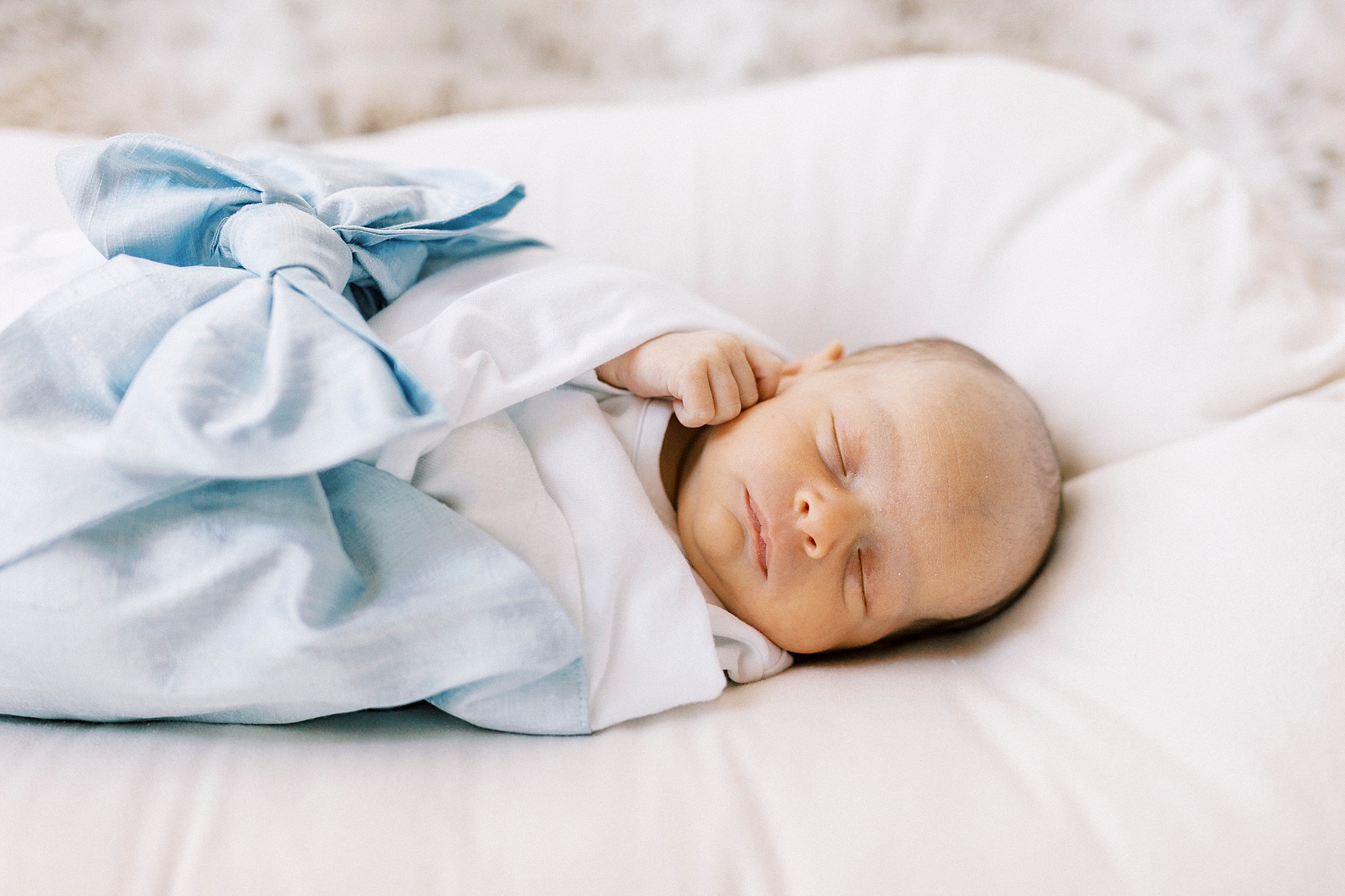 baby boy lays in blue blanket on white pillow during newborn photos