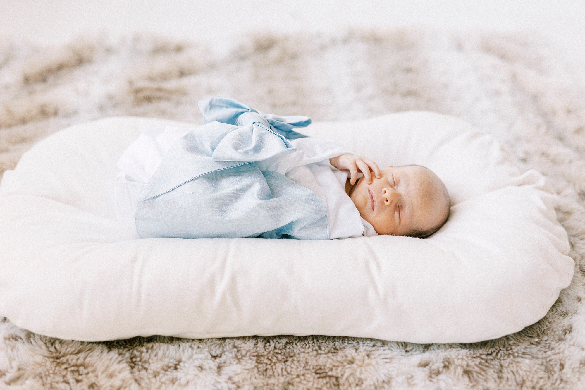 baby boy lays in blue blanket on white pillow during newborn photos