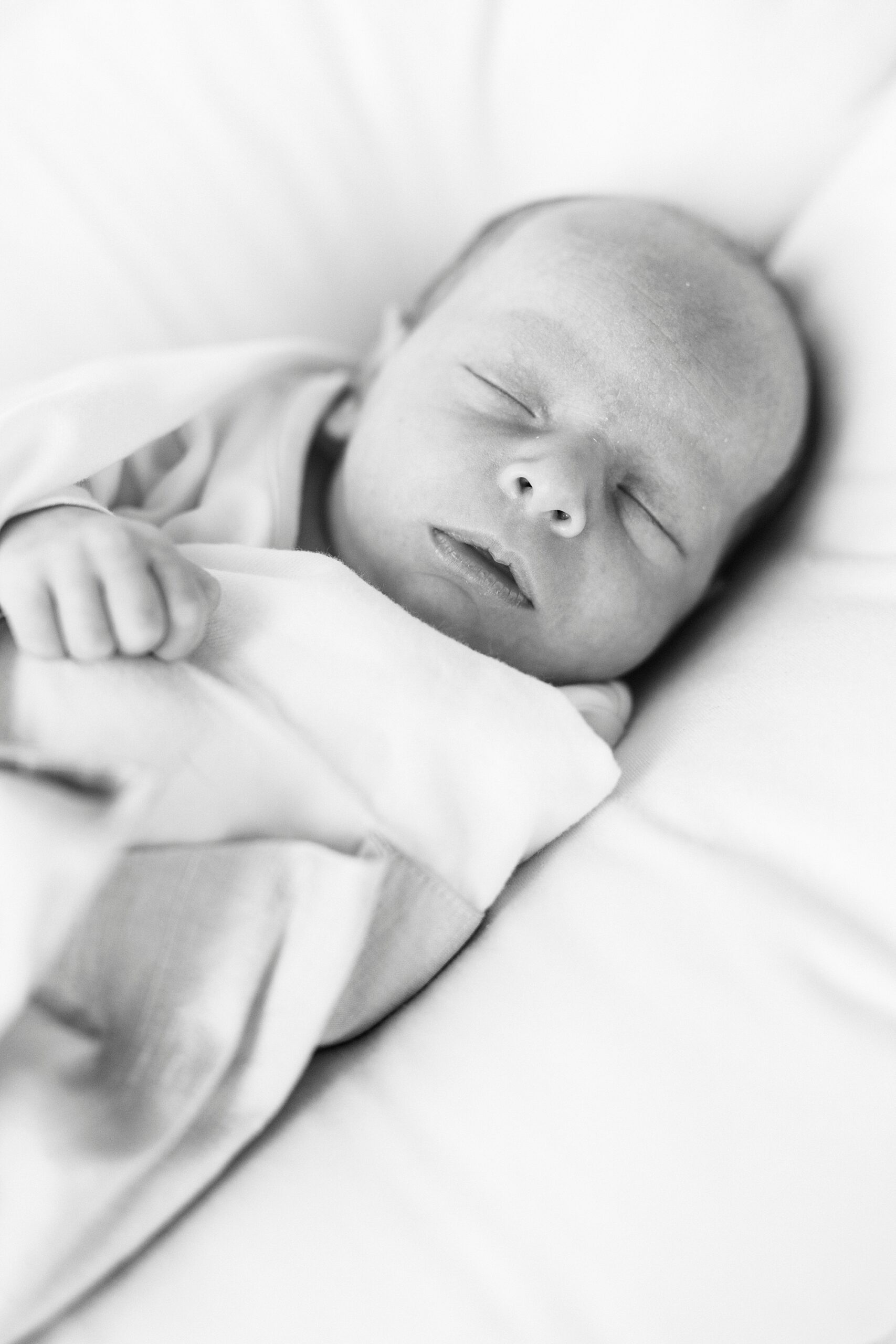 baby boy lays in blue blanket on white pillow during newborn photos