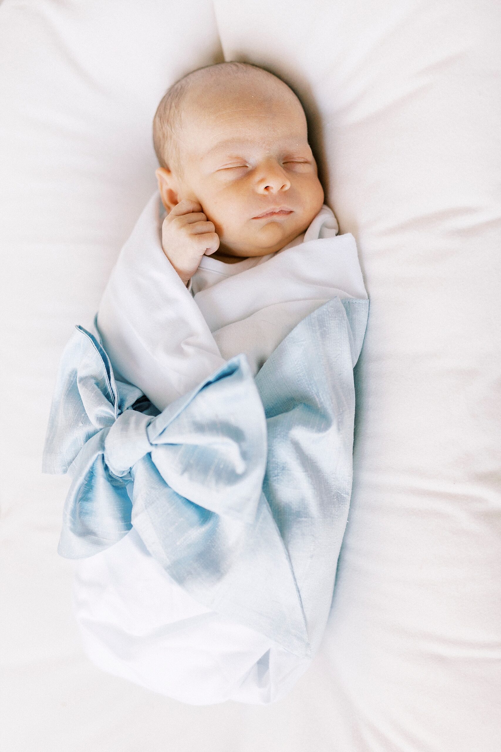 baby boy lays in blue blanket on white pillow during newborn photos