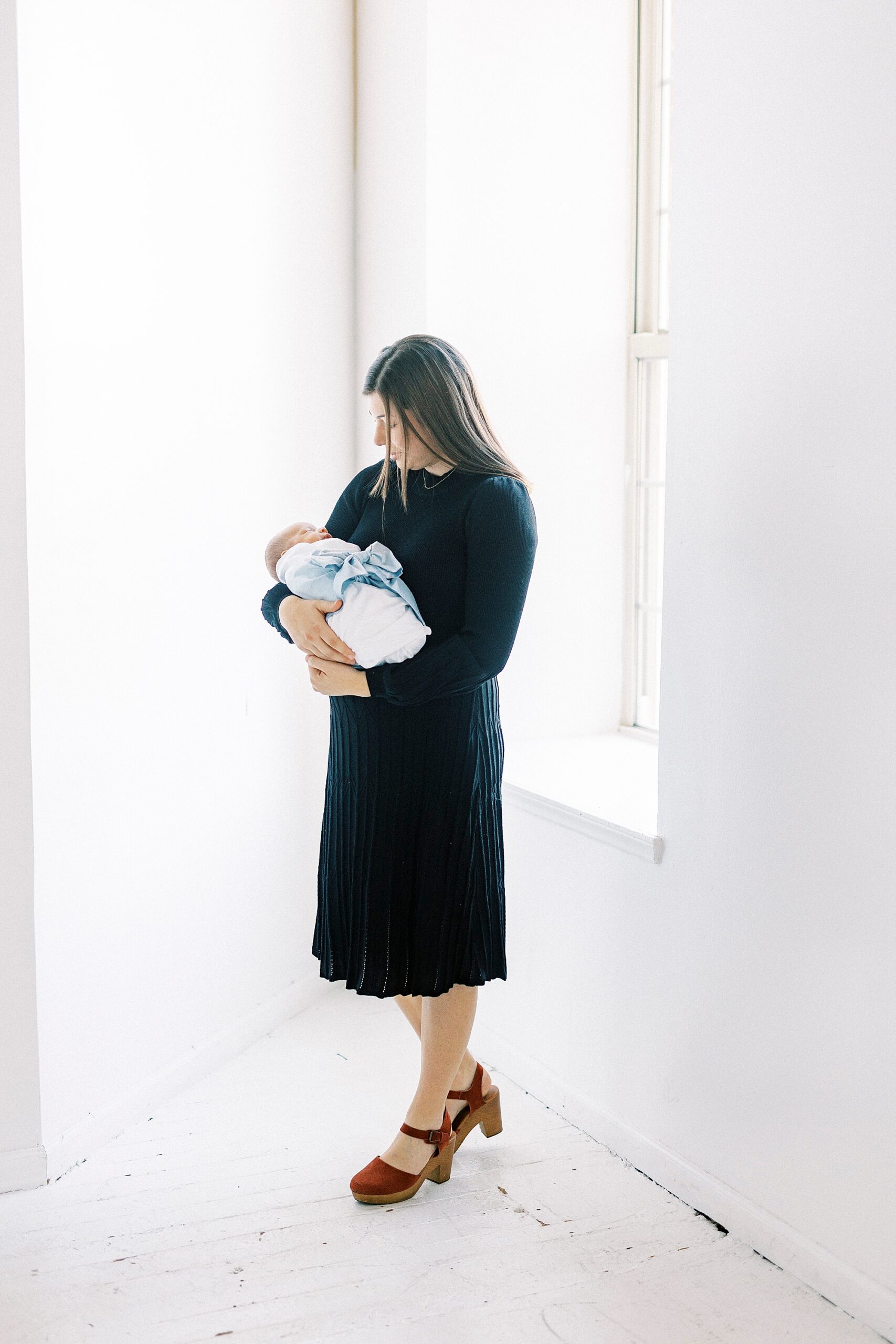 mom hugs newborn son in window during studio portraits in Concord NC