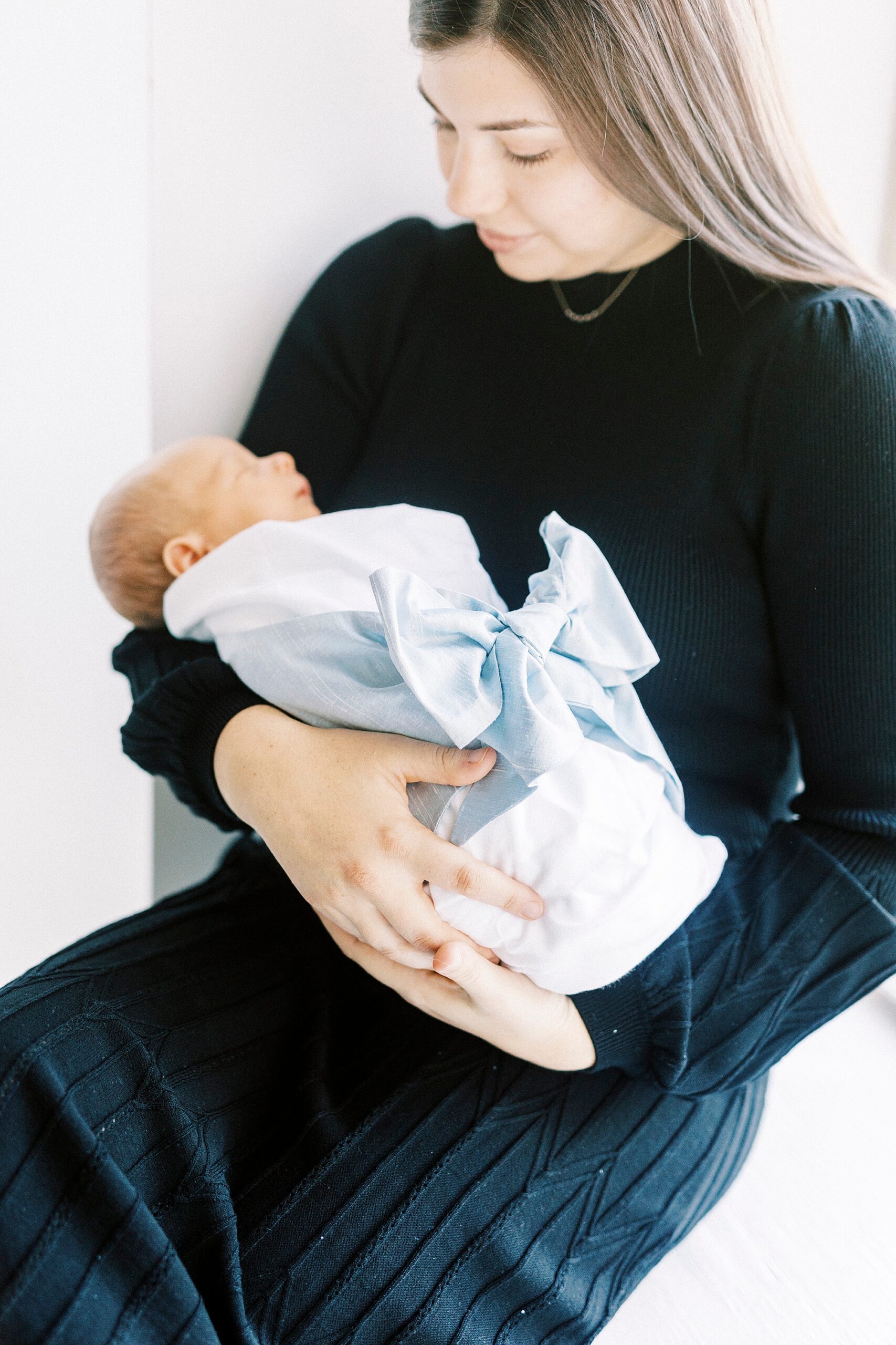woman holds son in white blanket with blue bow during studio portraits in Concord NC