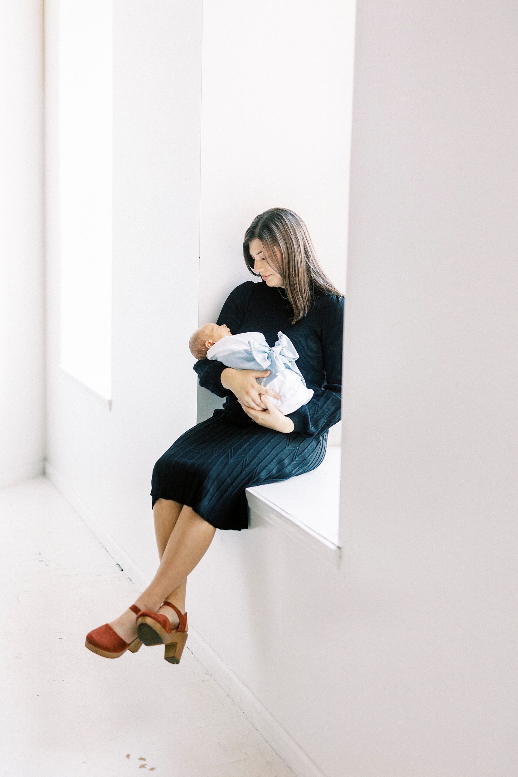 woman holds son in white blanket with blue bow during studio portraits in Concord NC
