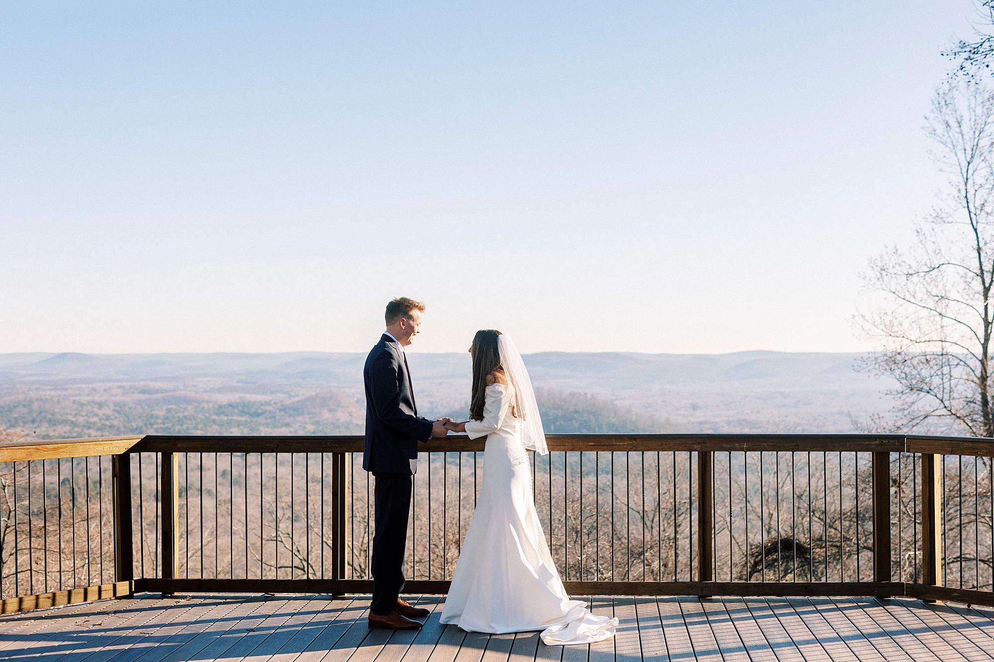 bride and groom hold hands near wooden railing on top of Morrow Mountain