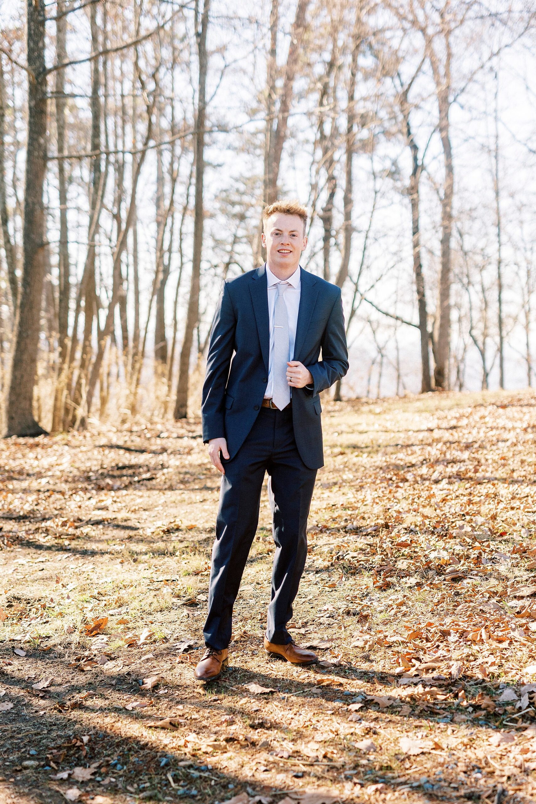 groom stands on side of hill in navy suit during portraits on Morrow Mountain