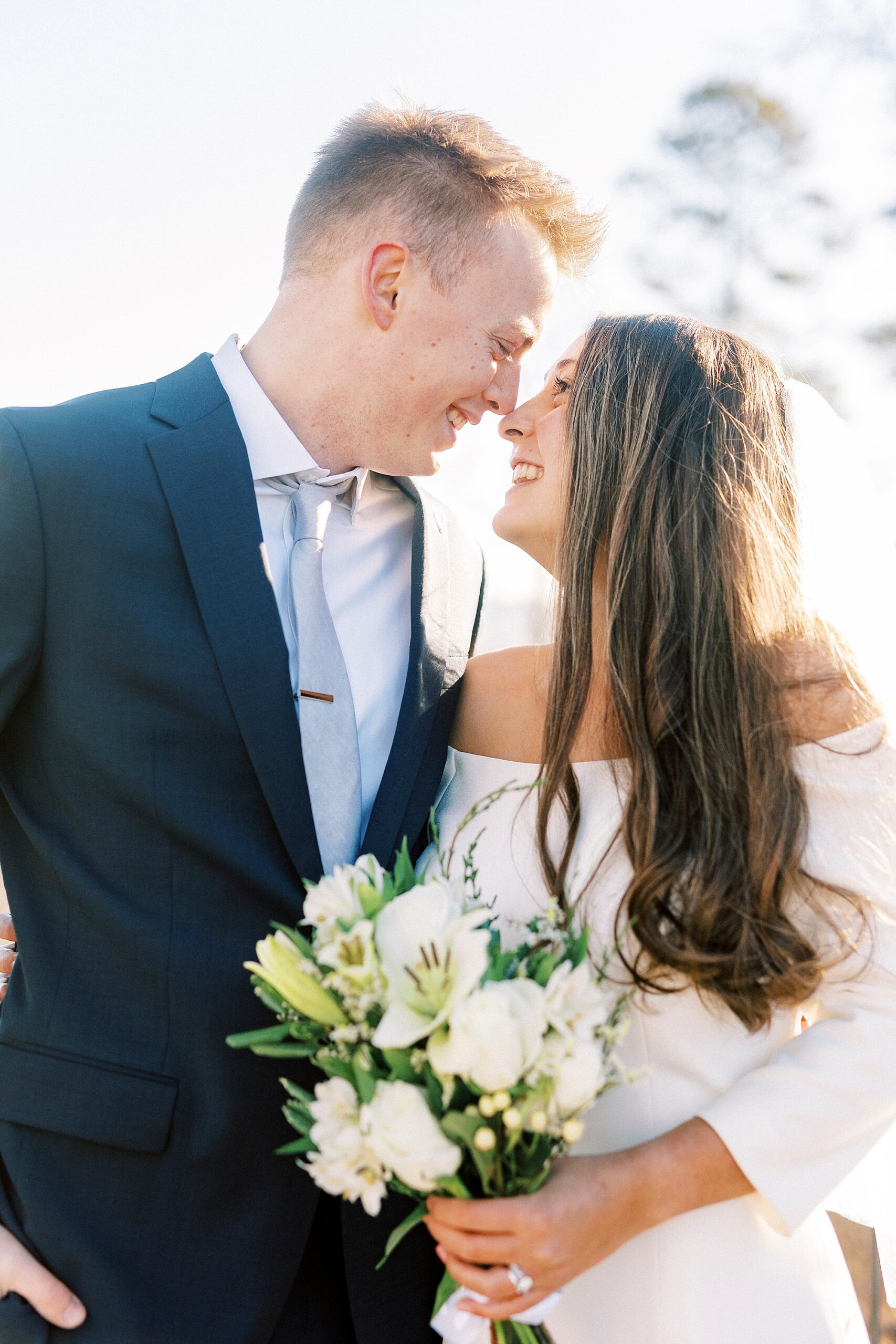 bride and groom lean together touching noses while bride holds bouquet of ivory flowers 