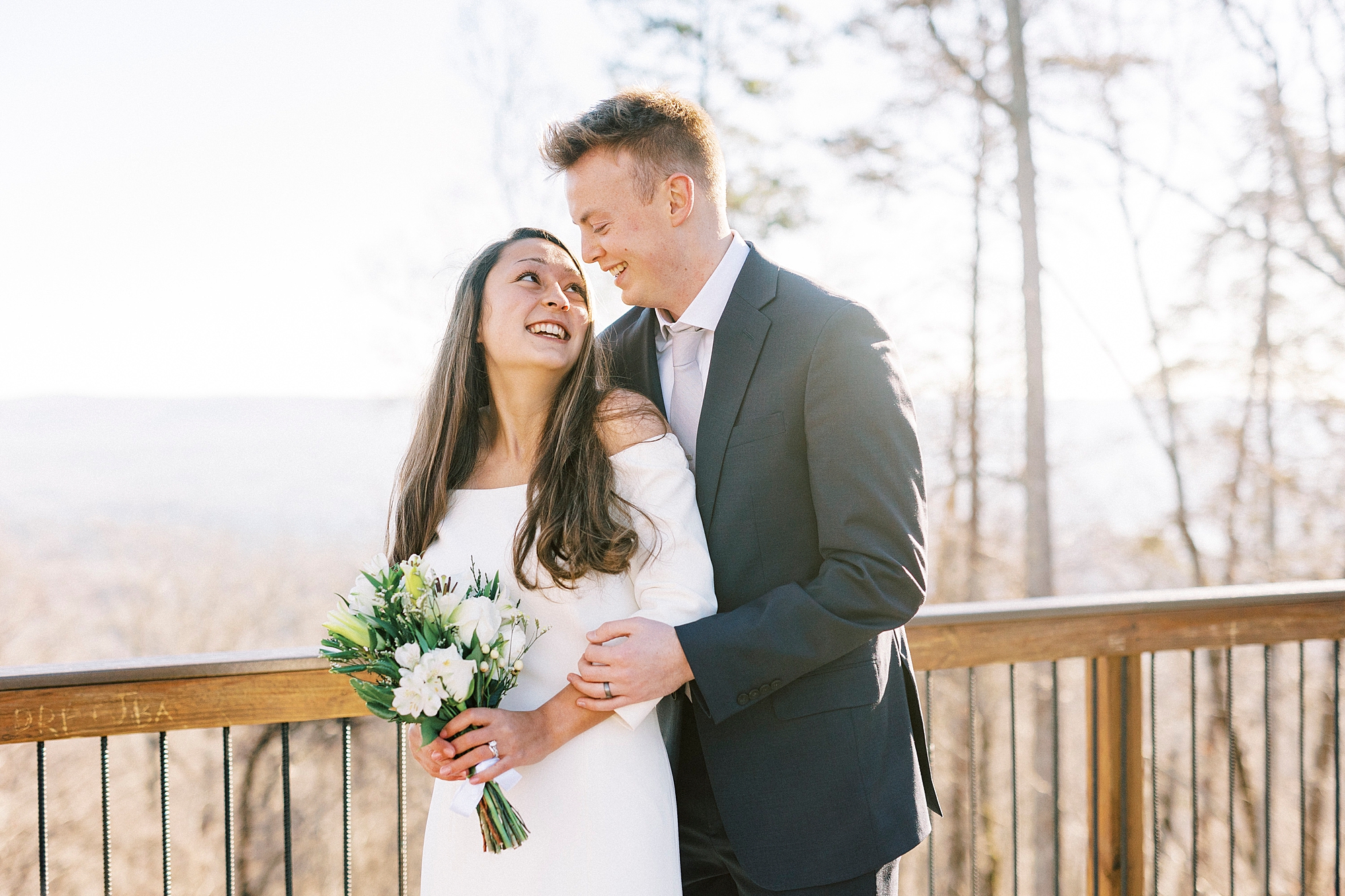 bride and groom hug on wooden railing on top of Morrow Mountain