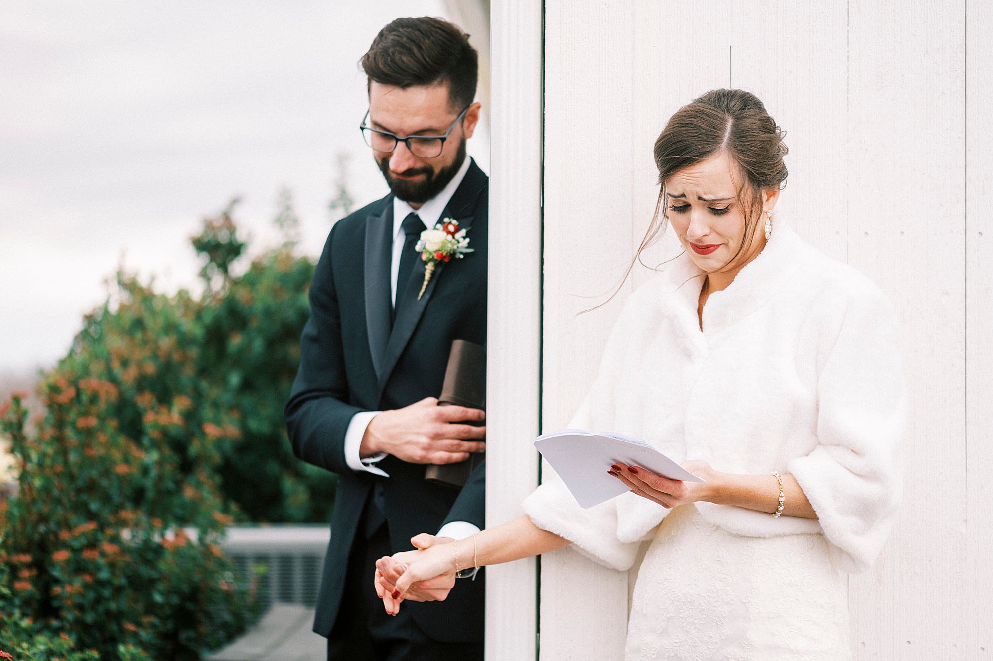 bride and groom hold hands exchanging letters around white door of Chickadee Hill Farms