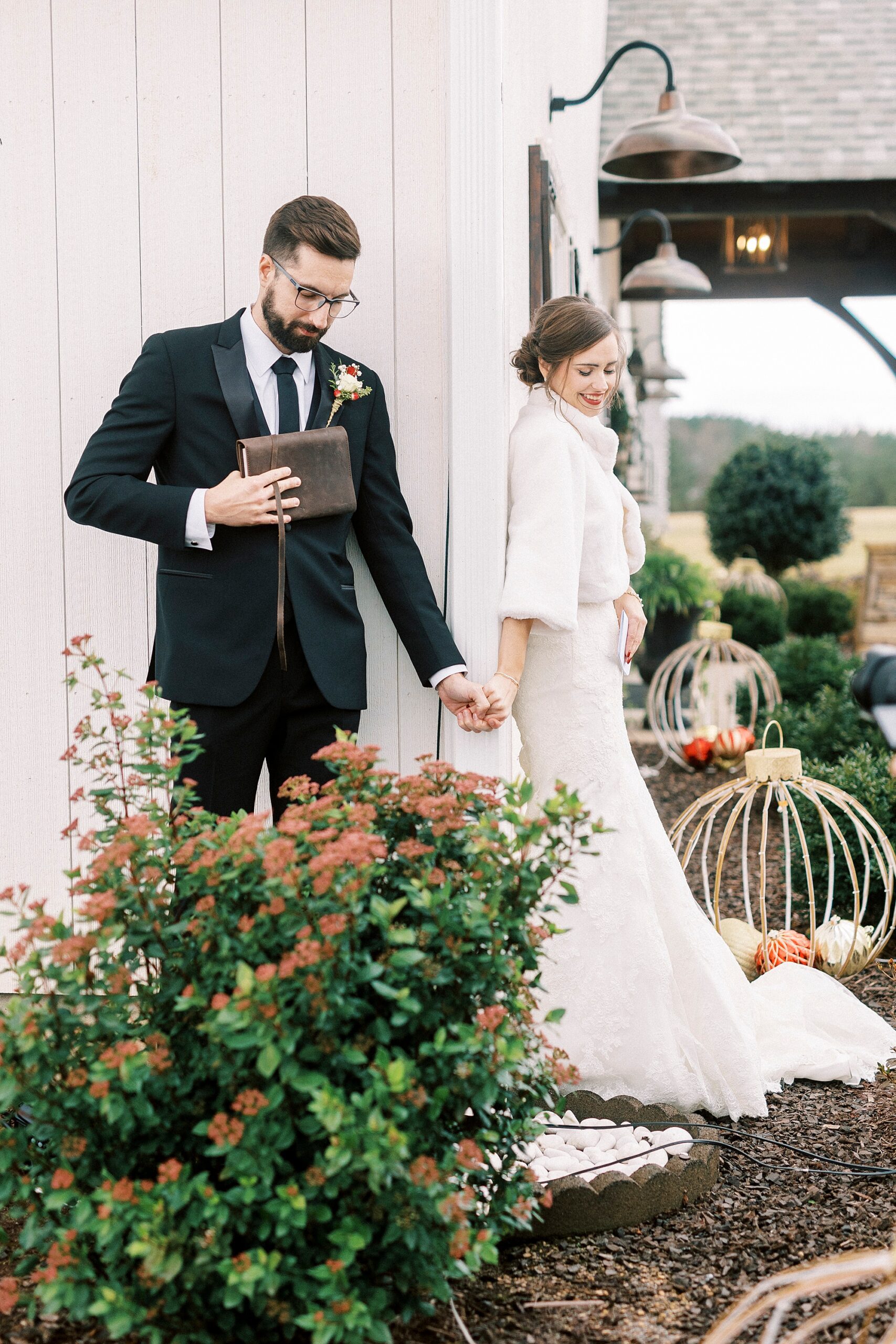 bride and groom hold hands around corner of Chickadee Hill Farms during first touch 