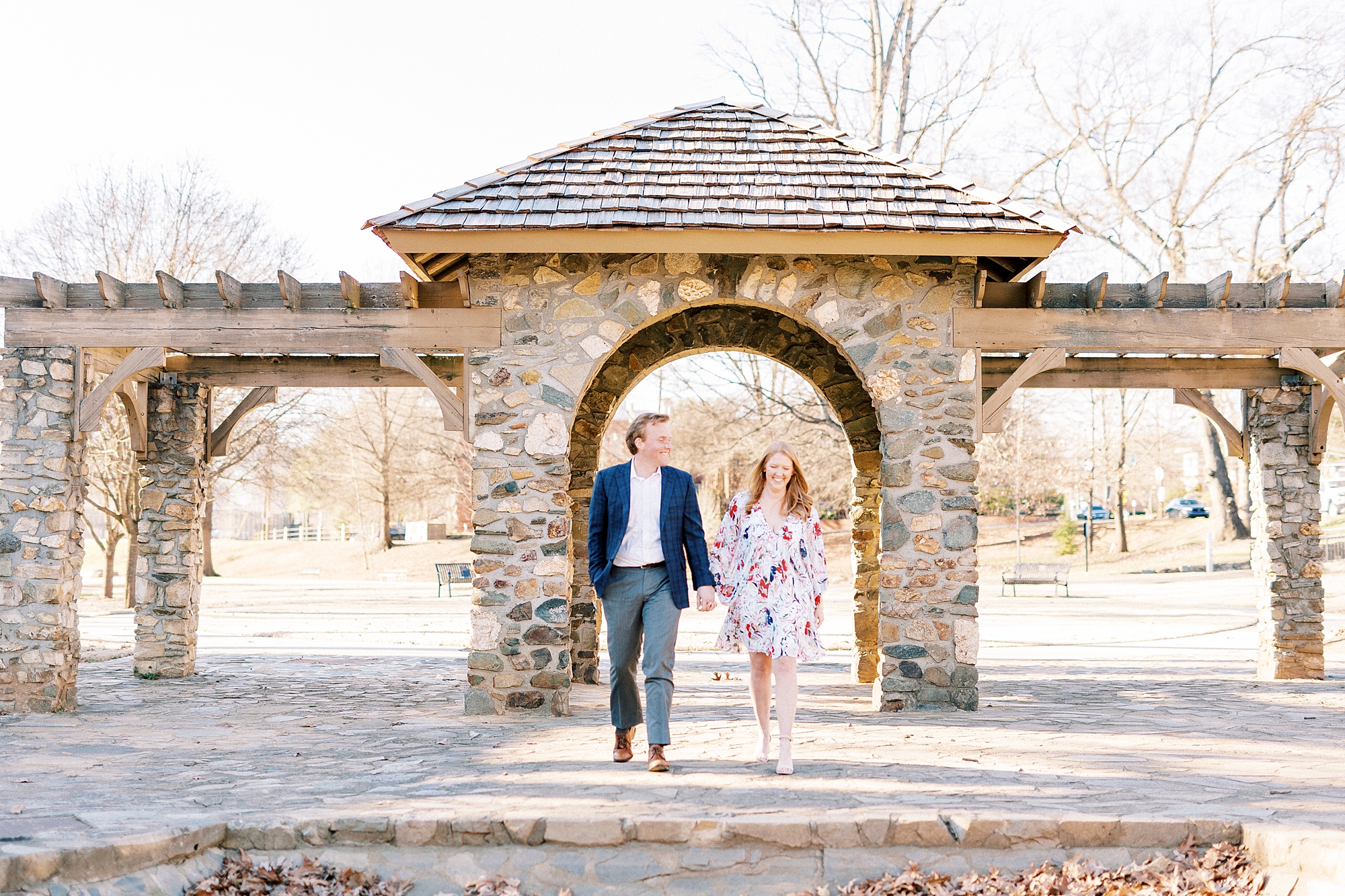 couple holds hands walking under brick structure in Independence Park
