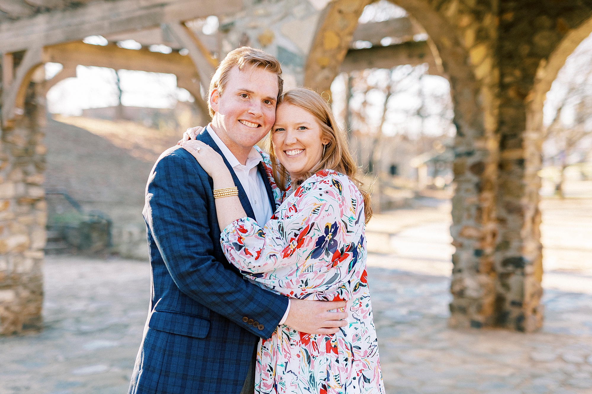 engaged couple hugs leaning heads together in front of stone arch at Independence Park