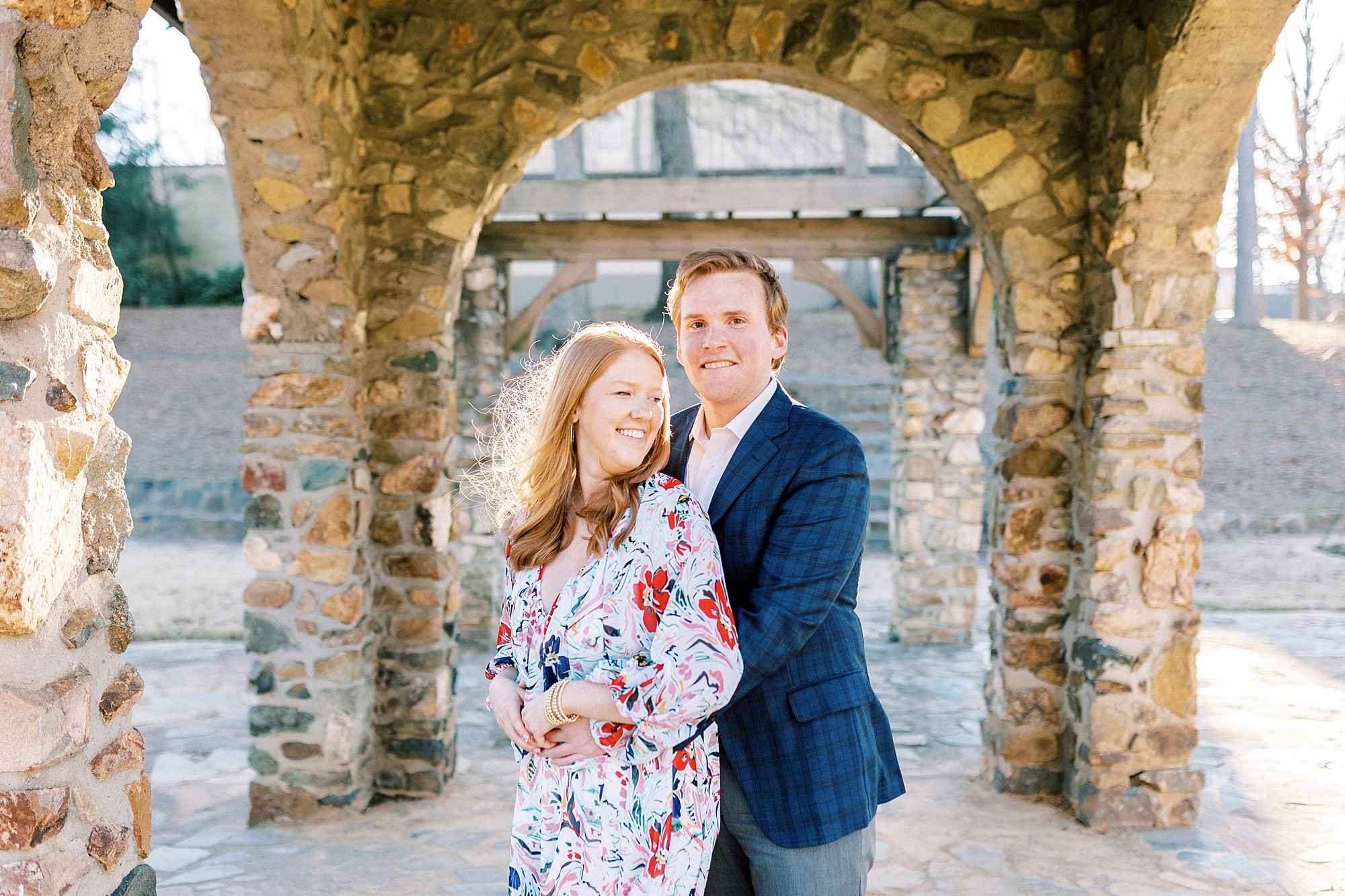 man hugs woman in floral dress in front of stone archway inside Independence Park