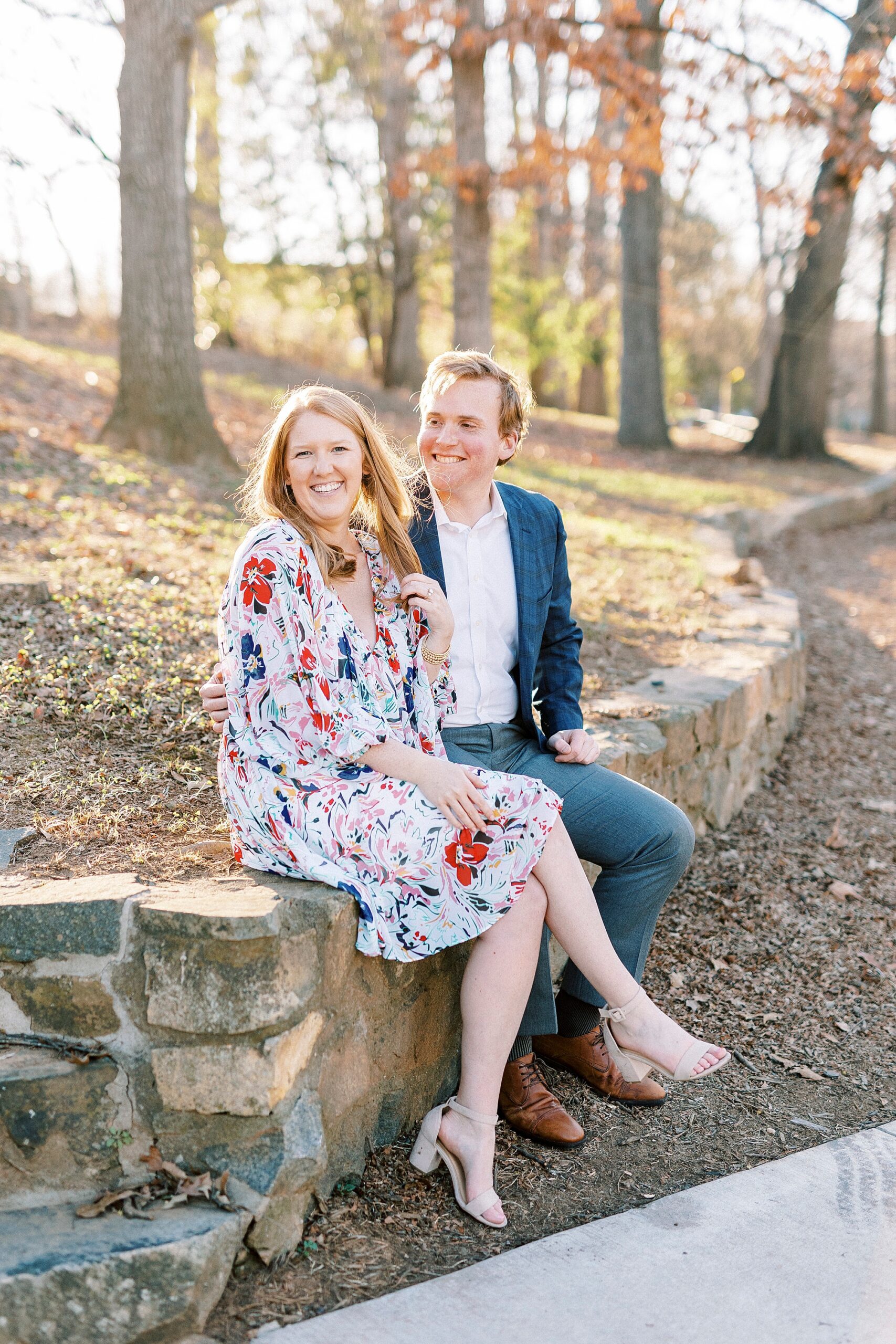 couple laughs sitting on wall inside Charlotte NC park