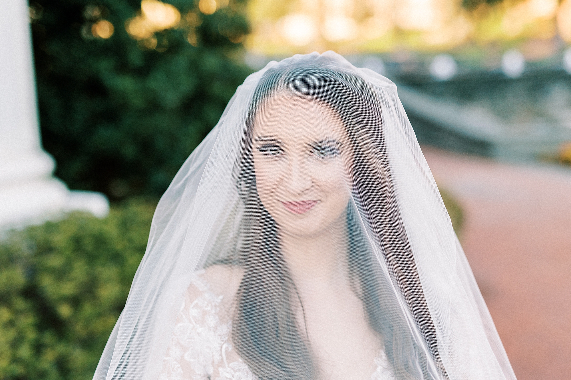 bride smiles under veil standing on brick walkways in Downtown Kannapolis